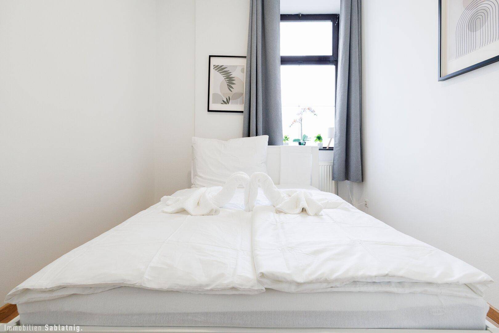 Einfaches Schlafzimmer mit Einzelbett, weißen Wänden und einem gerahmten Bild über dem Bett.