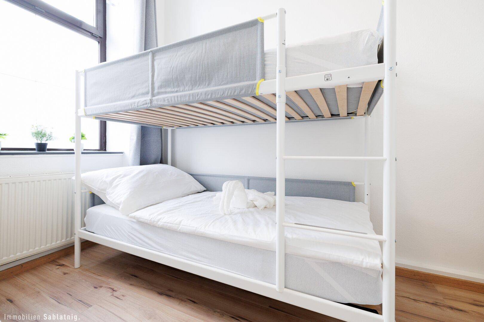 Nahaufnahme eines Etagenbettes in einem Schlafzimmer mit Fenster und Heizung im Hintergrund.