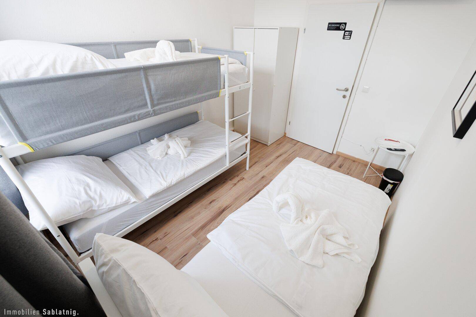 Geräumiges Schlafzimmer mit Etagenbett und Einzelbett, Holzboden und weißem Kleiderschrank.