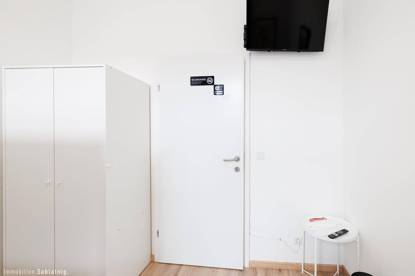 Weißer Kleiderschrank und Tür in einem Schlafzimmer mit Wandfernseher und kleinem Beistelltisch.