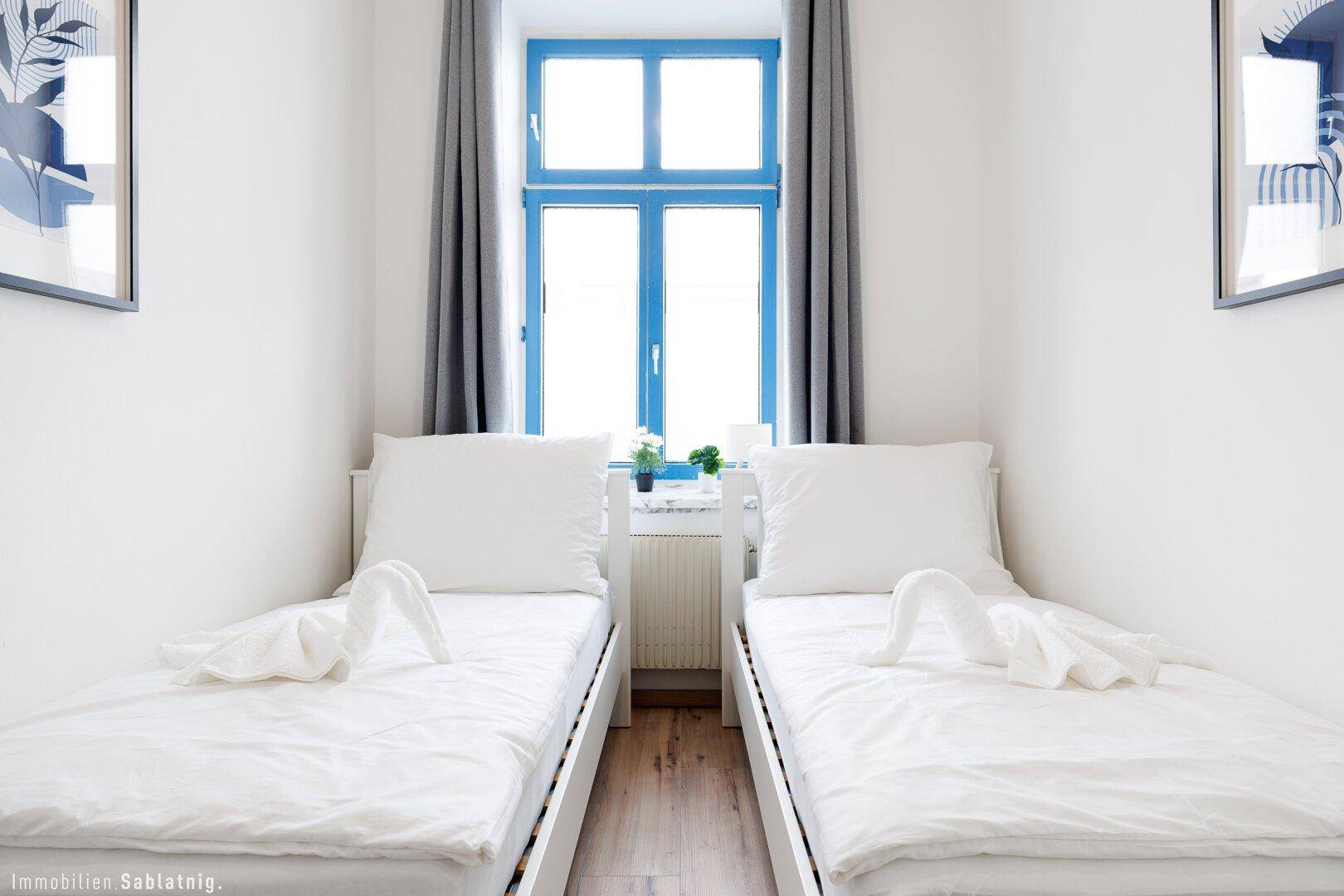 Nahaufnahme von zwei Einzelbetten in einem Schlafzimmer mit blau gerahmtem Fenster.
