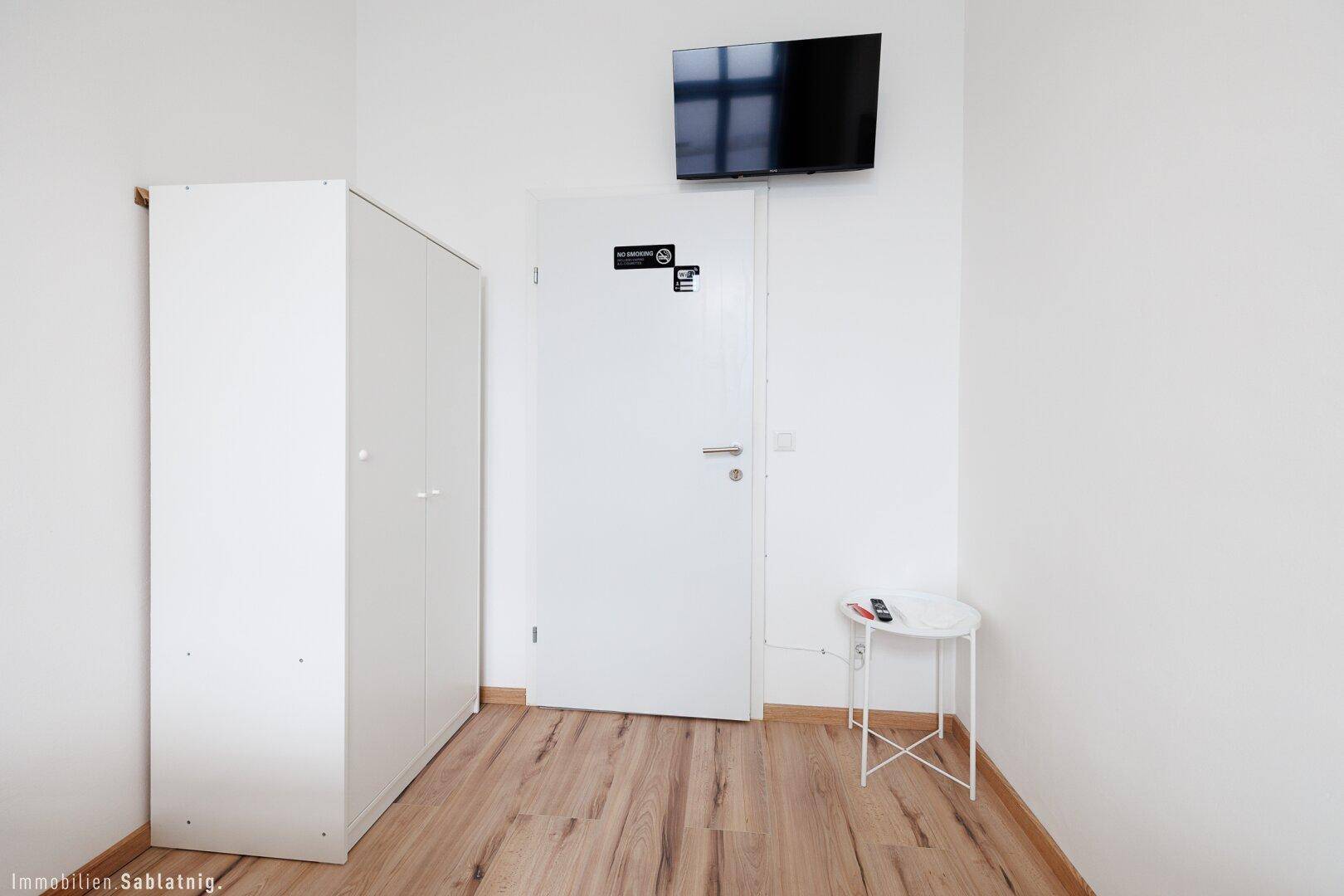 Weißer Kleiderschrank und Tür in einem Schlafzimmer mit Wandfernseher und kleinem Beistelltisch.