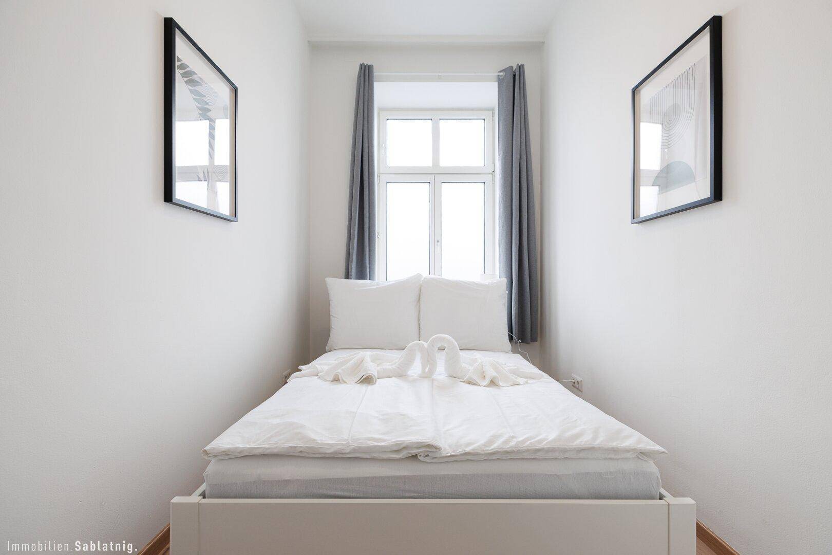 Gemütliches Schlafzimmer mit Doppelbett, Holzboden und einem Fenster, das viel Tageslicht hereinlässt.