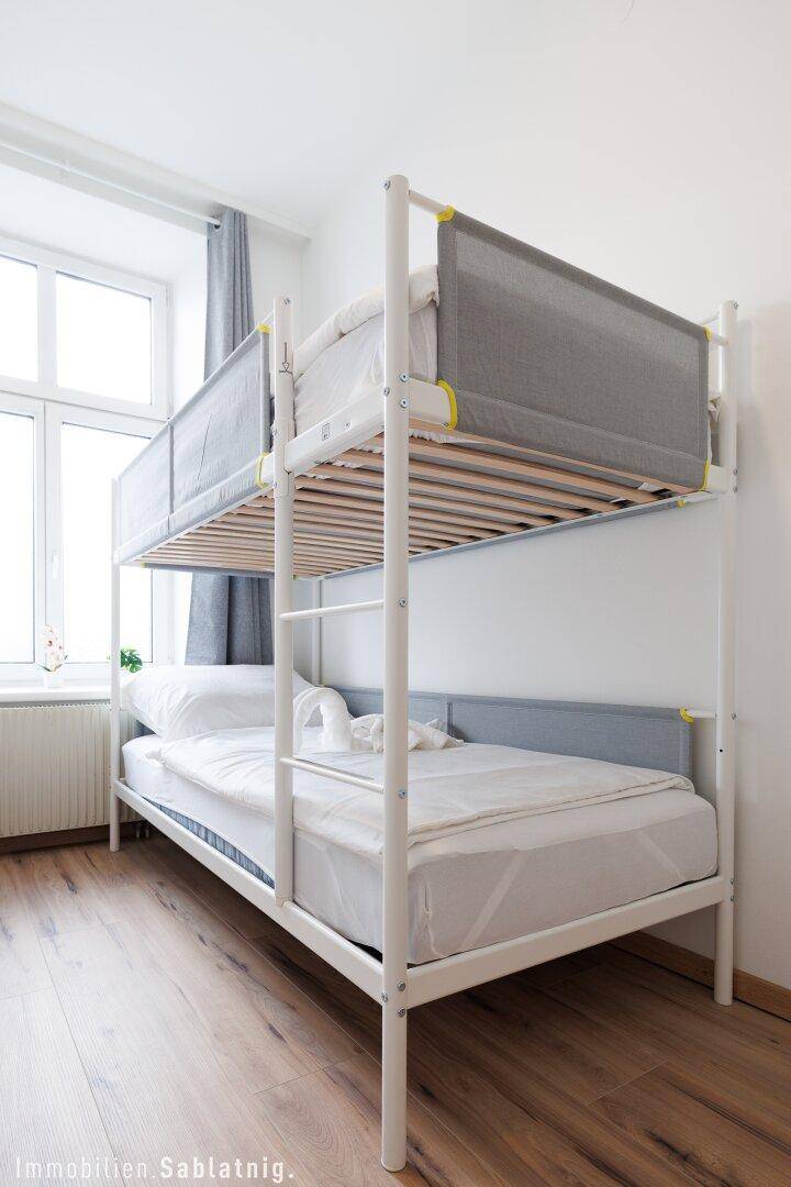 Detailansicht eines Etagenbettes in einem hellen Schlafzimmer mit Holzboden und Fenster.