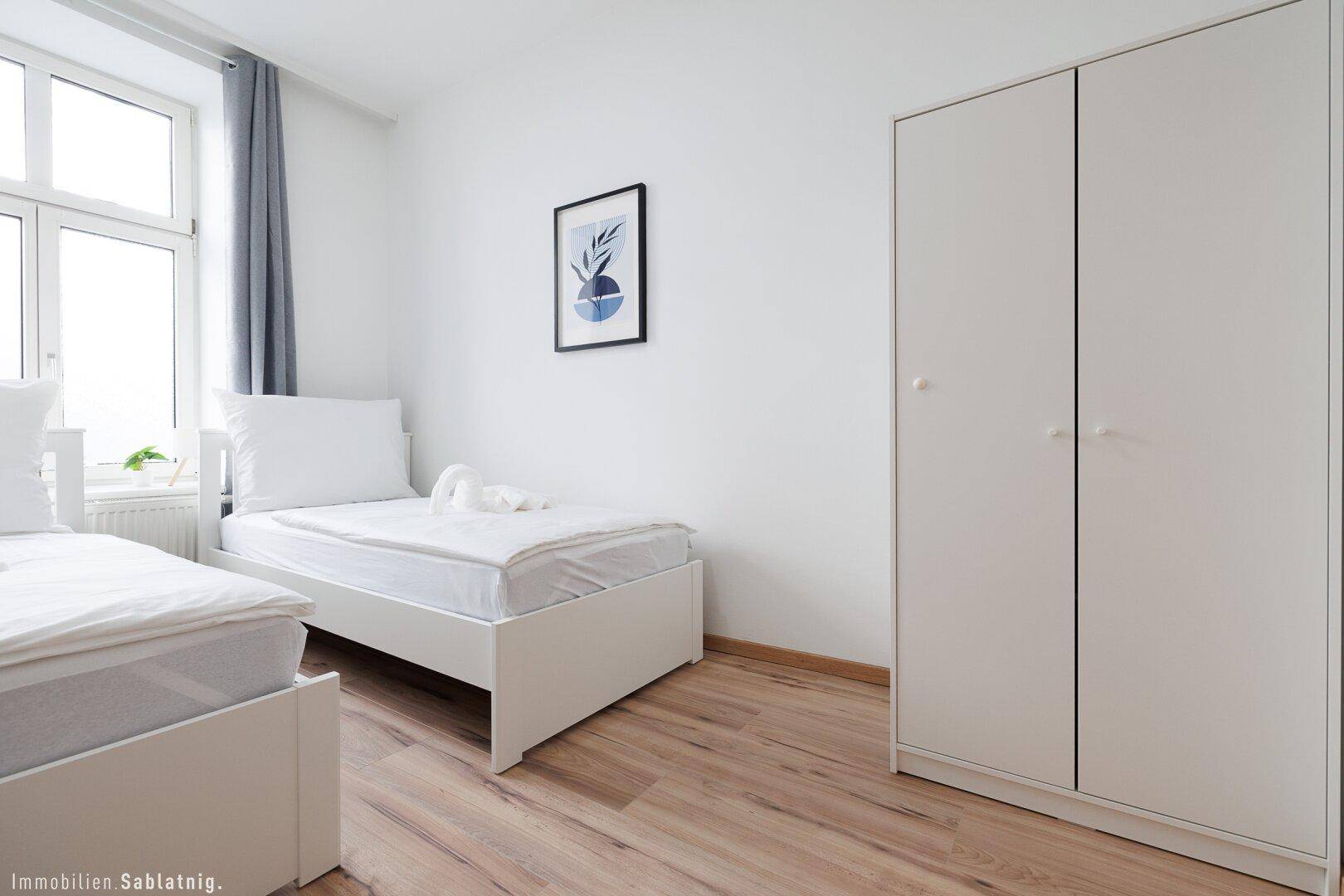 Schlafzimmer mit zwei Einzelbetten, Holzboden und einem weißen Kleiderschrank.
