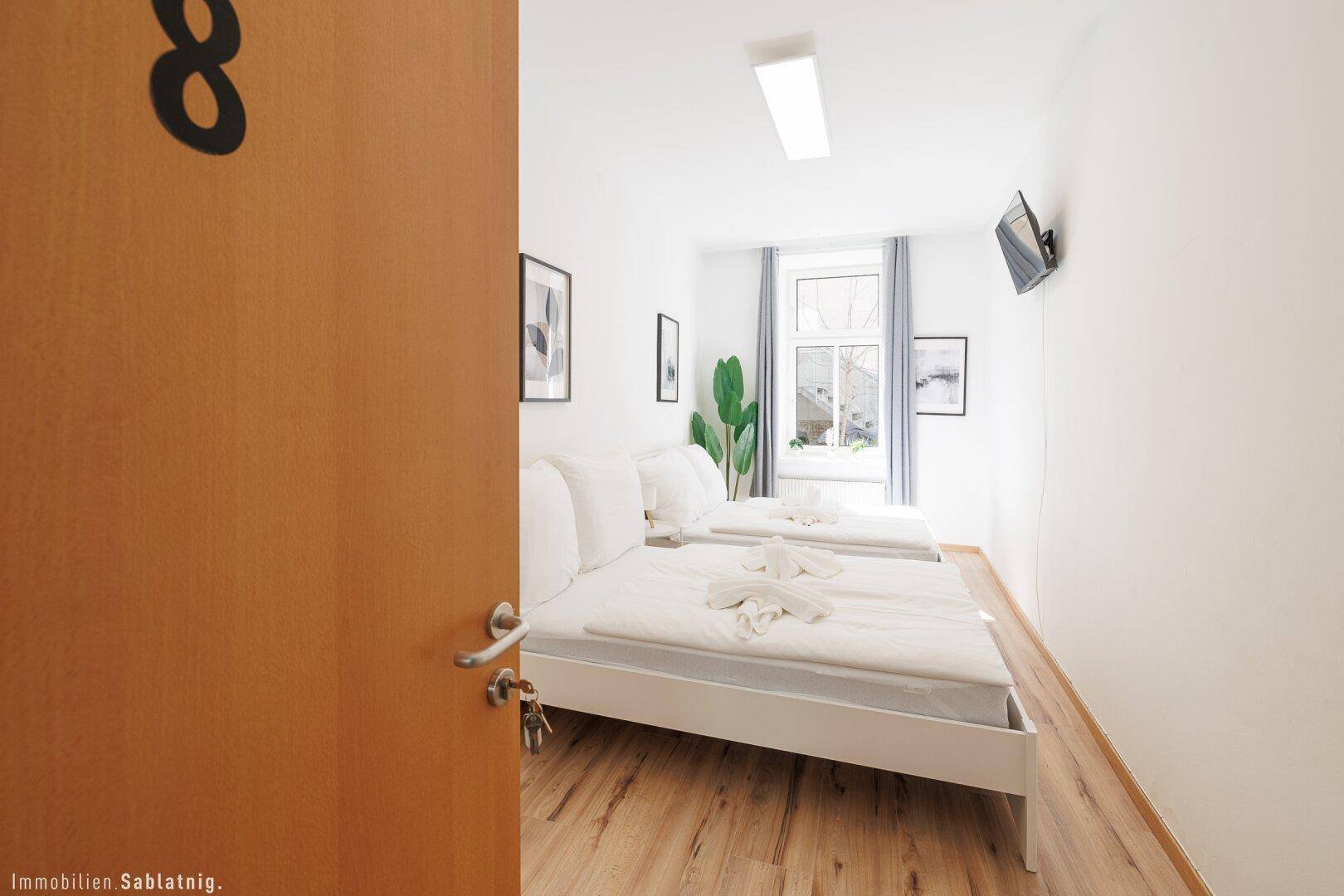 Schlafzimmer mit zwei Einzelbetten, Holzboden und einem Fenster mit grauen Vorhängen.
