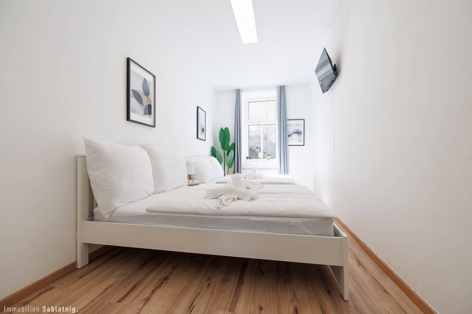 Helles Schlafzimmer mit zwei Einzelbetten, Holzboden und einem Fenster, das viel Tageslicht hereinlässt.
