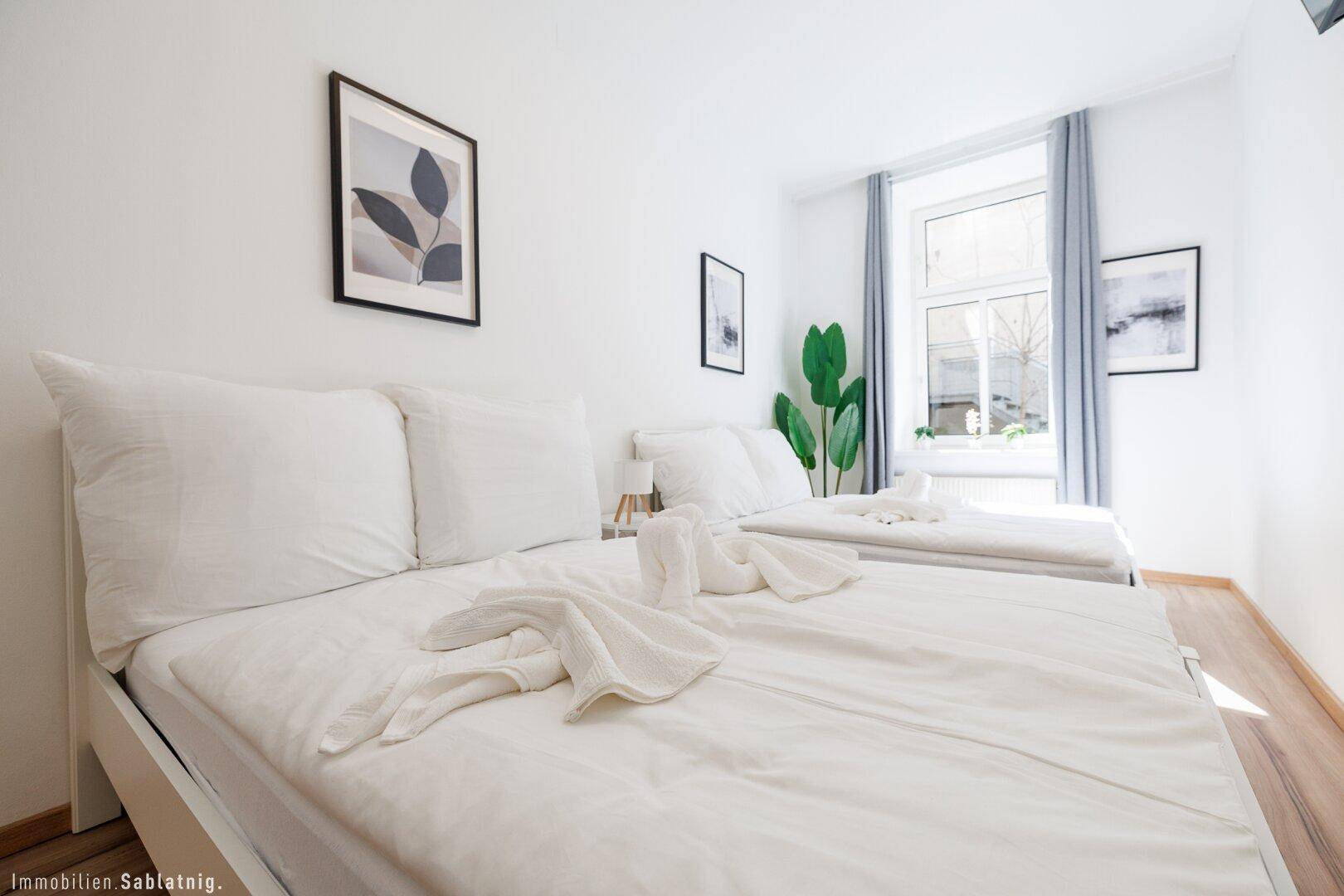 Schlafzimmer mit zwei Einzelbetten, Holzboden und einer großen Pflanze als Dekoration.