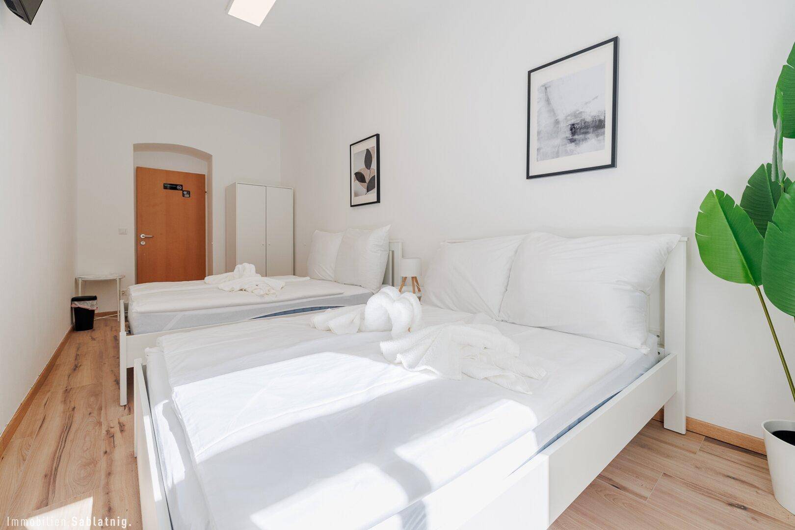 Schlafzimmer mit zwei Einzelbetten, Holzboden, einem Kleiderschrank und einer Holztür.