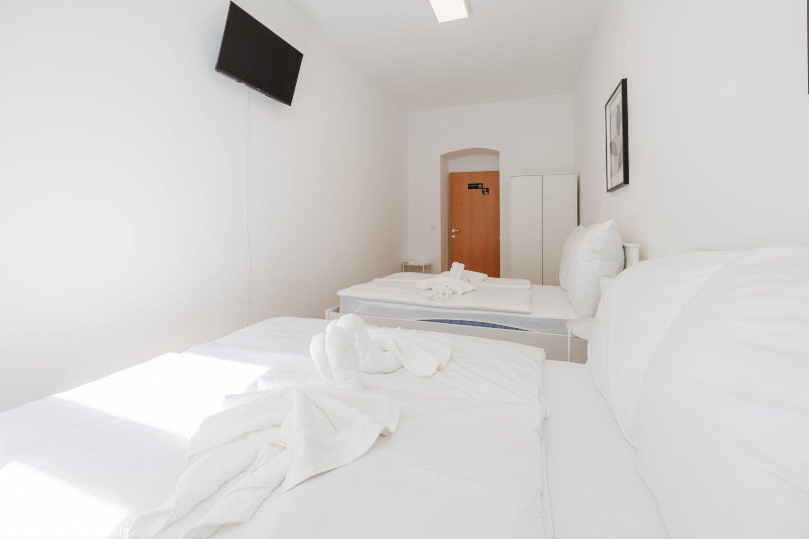 Helles Schlafzimmer mit zwei Einzelbetten, einem Wandfernseher und einfacher, funktionaler Einrichtung.