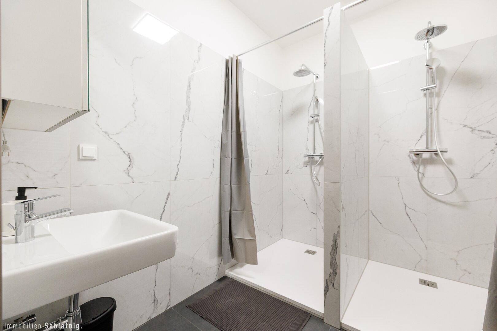 Modernes Badezimmer mit Waschbecken, Spiegelschrank und zwei Duschkabinen mit Marmorfliesen.