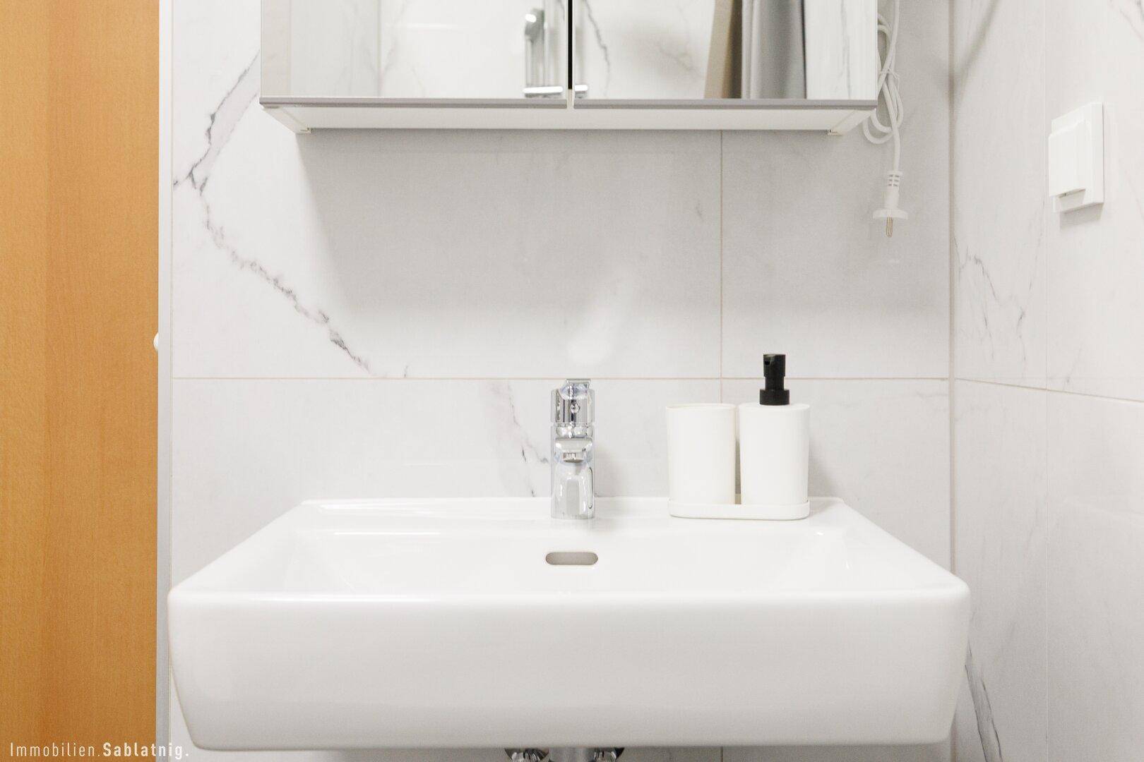 Nahaufnahme eines modernen Waschbeckens mit Armatur und Seifenspender in einem hellen Badezimmer.