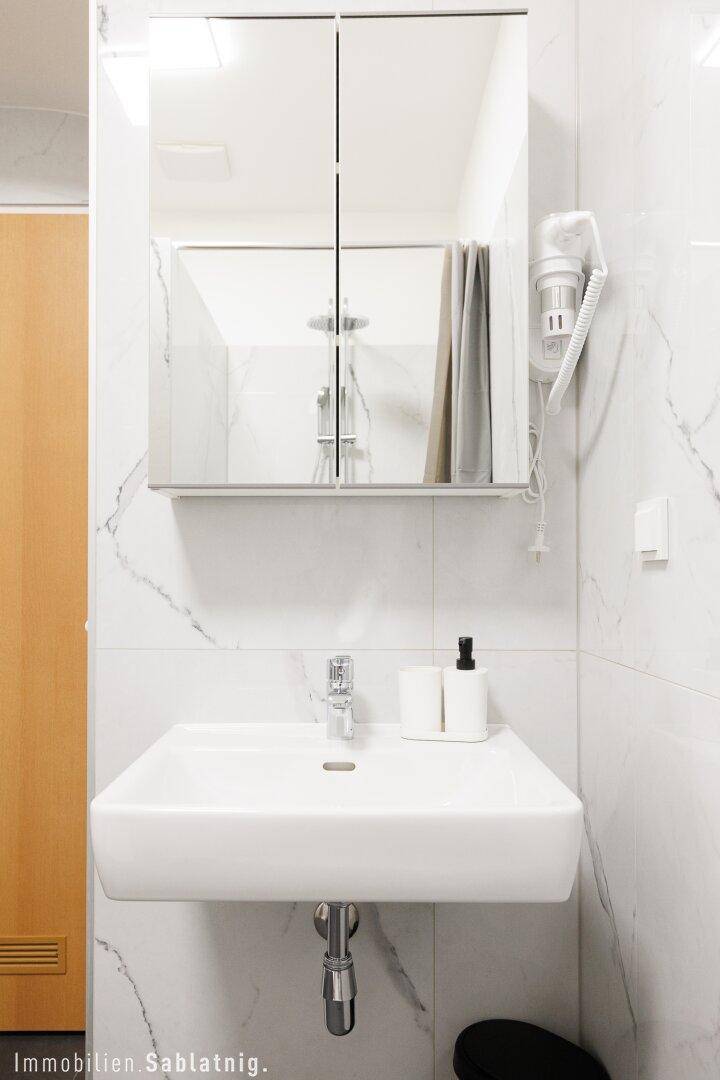 Nahaufnahme eines modernen Waschbeckens mit Spiegelschrank, der die Duschkabinen reflektiert.