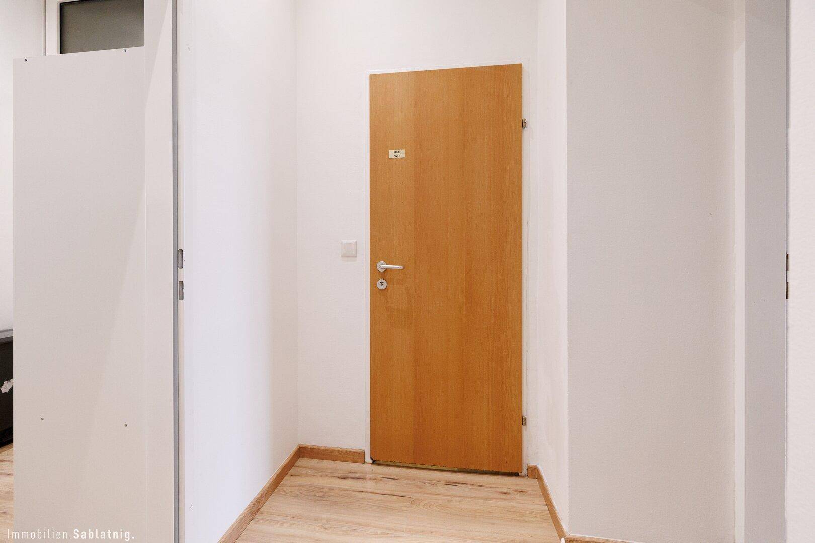 Heller Flur mit Holzboden und einer Holztür, die zu einem Badezimmer führt, sehr gepflegt.