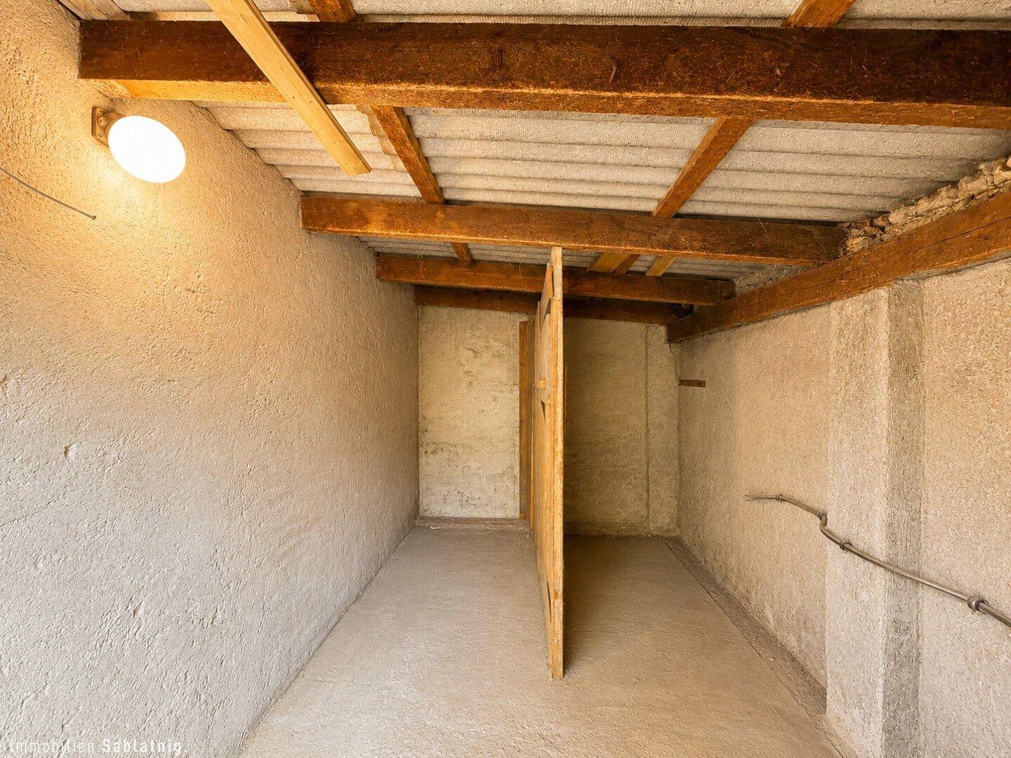 Unausgebauter Lagerbereich mit sichtbaren Holzbalken und einfacher Beleuchtung.