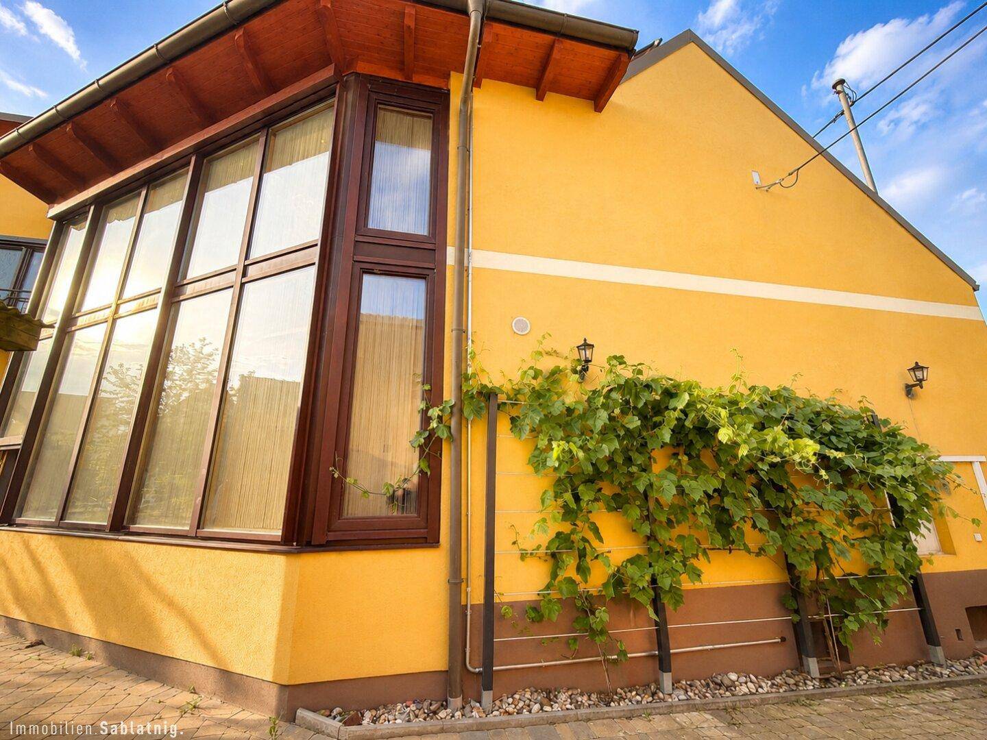 Seitenansicht des Hauses mit großer Glasfassade und Kletterpflanzen an der gelben Wand.