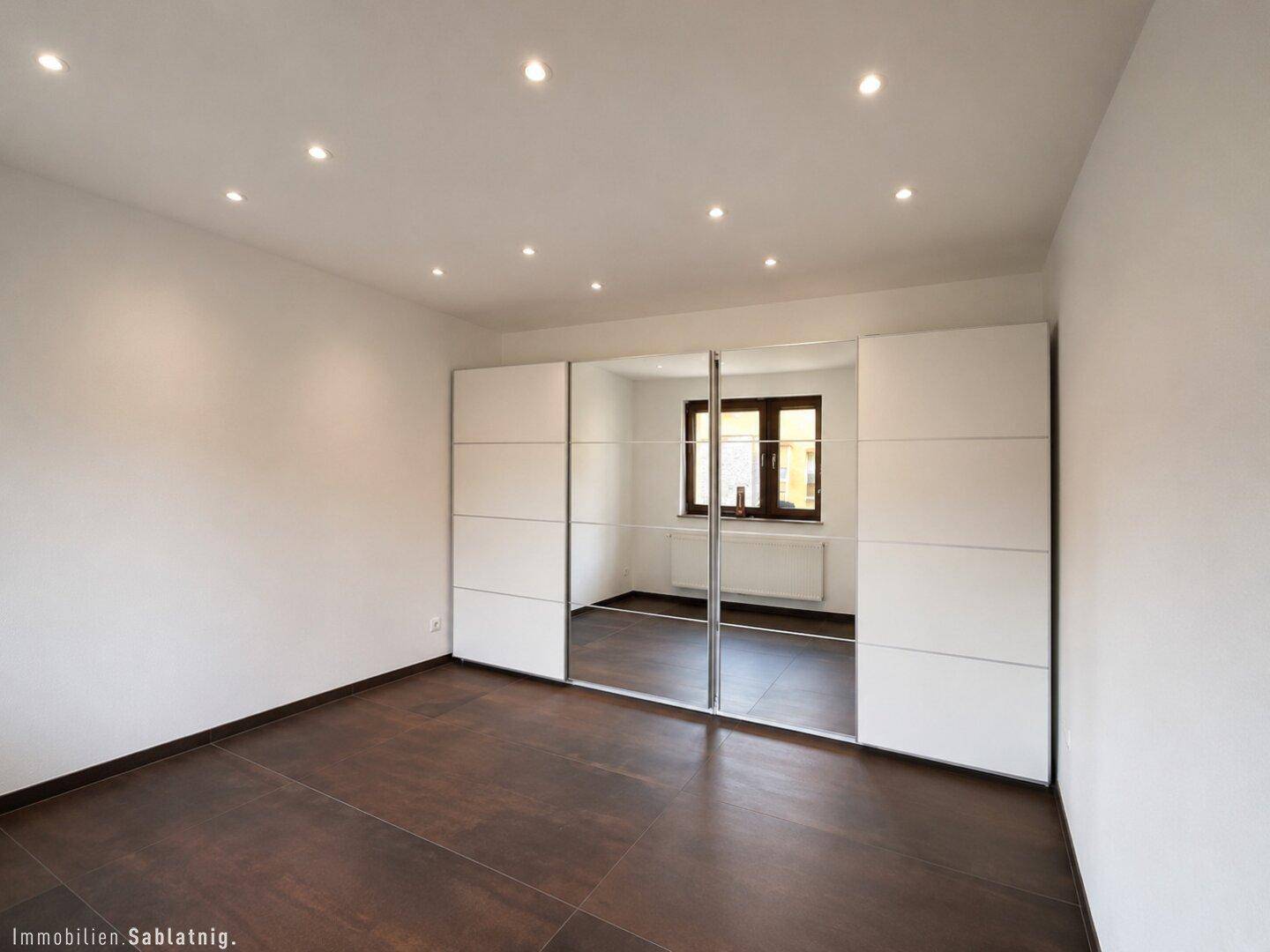Schlafzimmer mit dunklem Fliesenboden und großem Spiegelschrank.