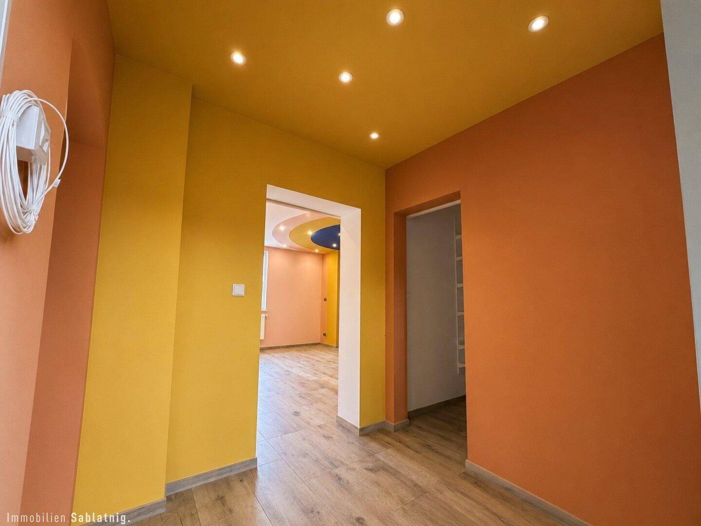 Heller Flur mit farbenfrohen Wänden in Gelb- und Orangetönen und Holzboden.