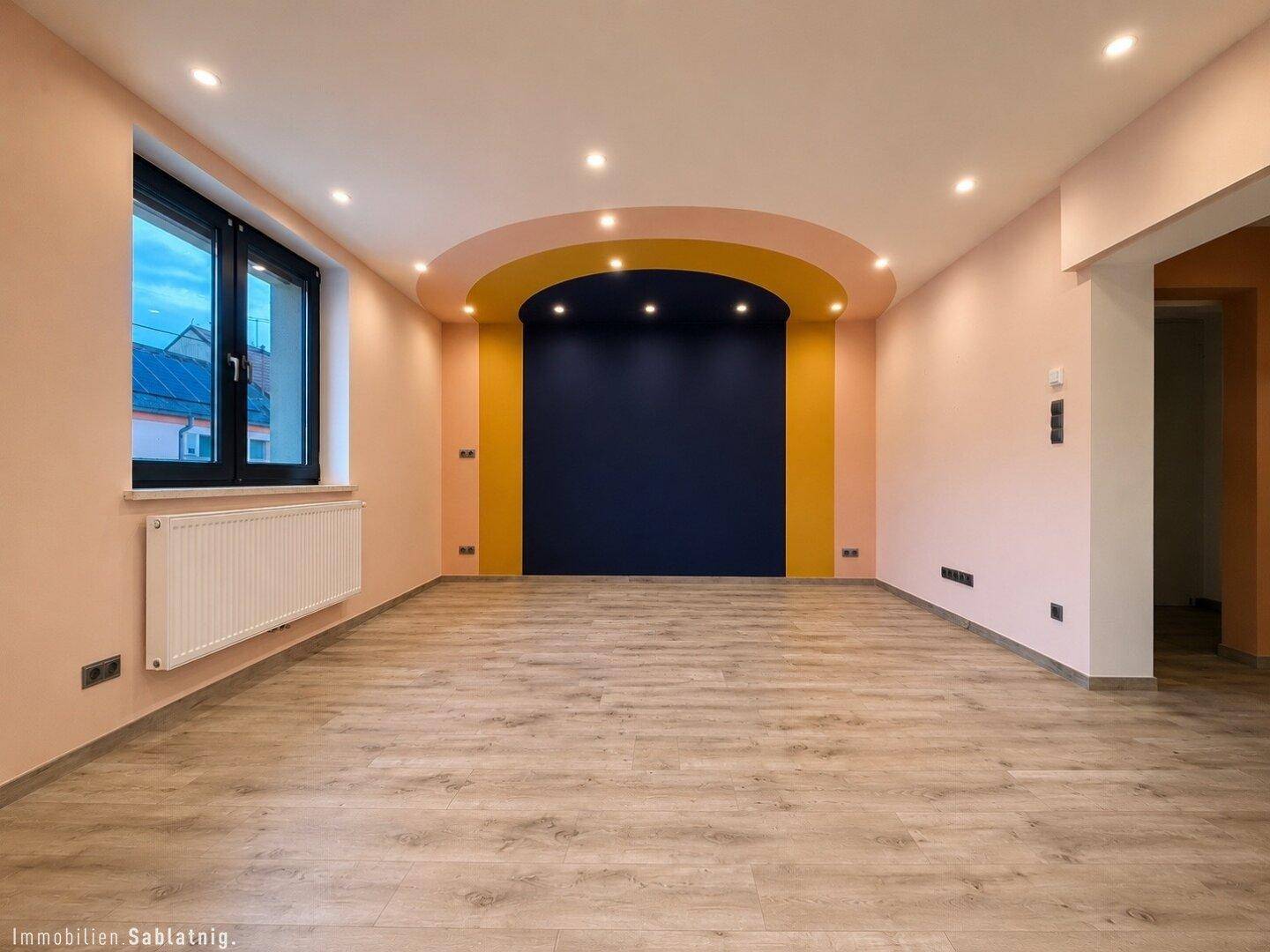 Wohnzimmer mit farbiger Akzentwand, Holzboden und integrierter Deckenbeleuchtung.