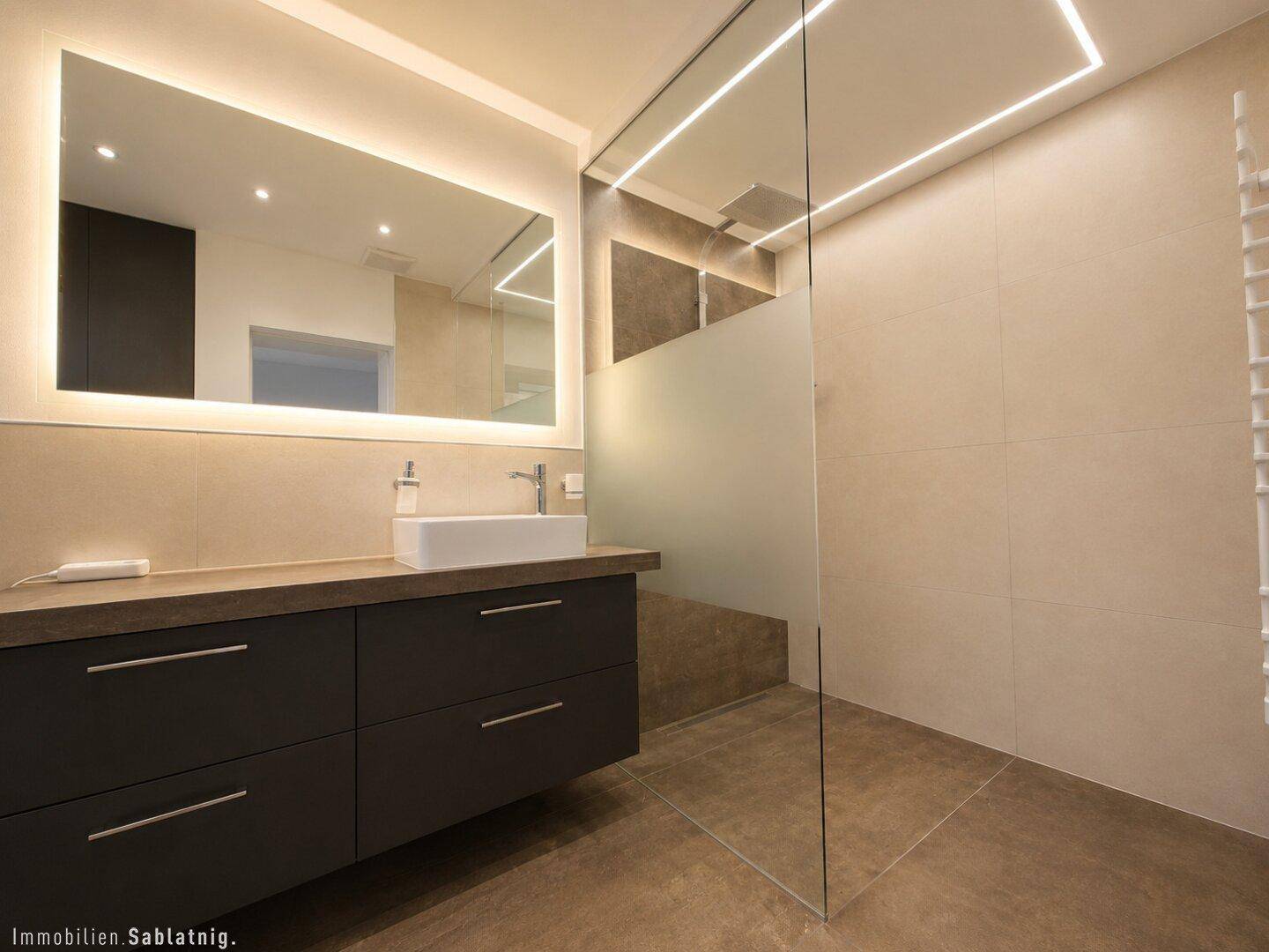 Modernes Badezimmer mit begehbarer Dusche, großem Spiegel und dunklen Möbeln.
