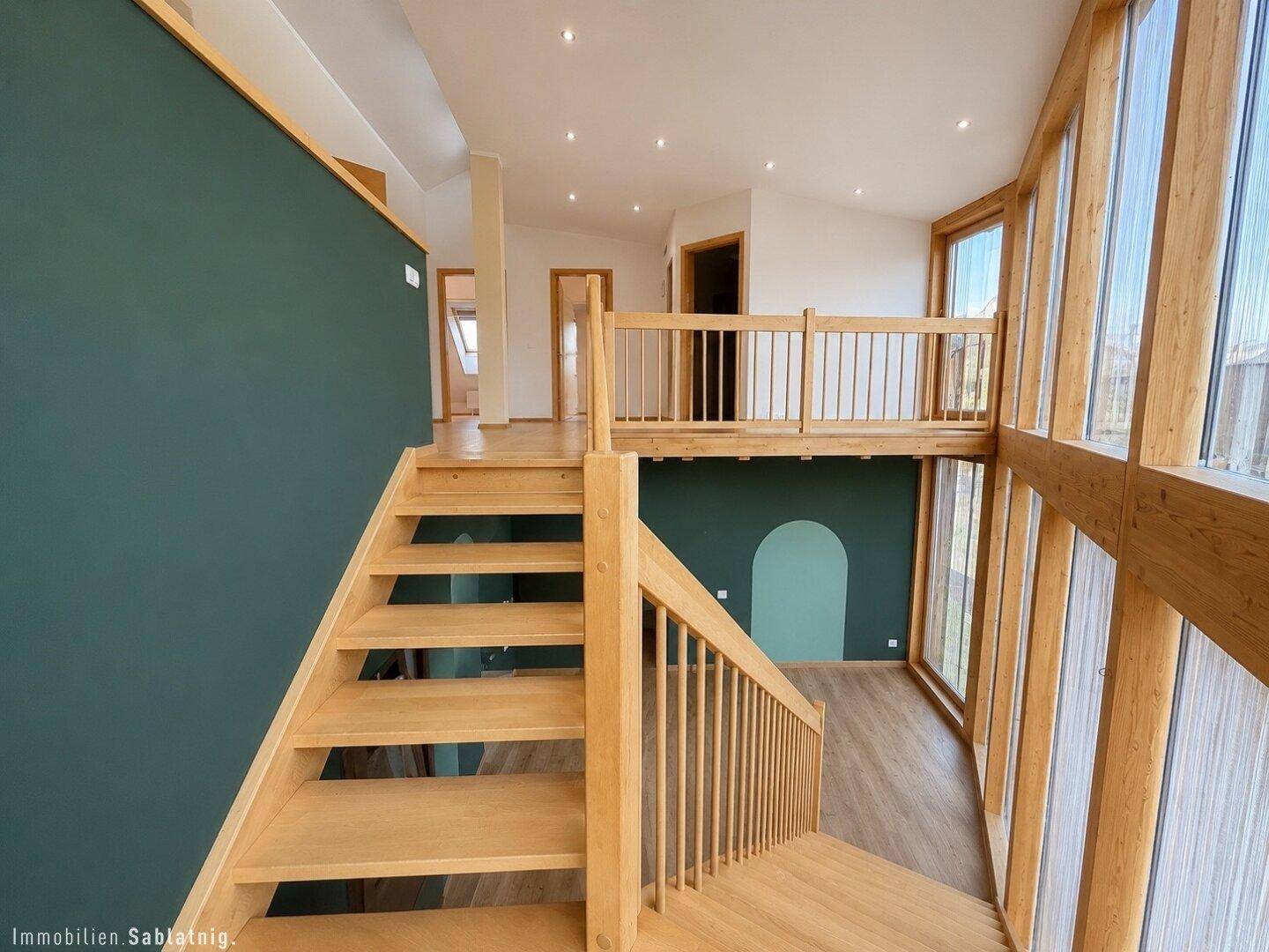 Offener Galeriebereich mit Holztreppe, hohen Decken und großen Fenstern.