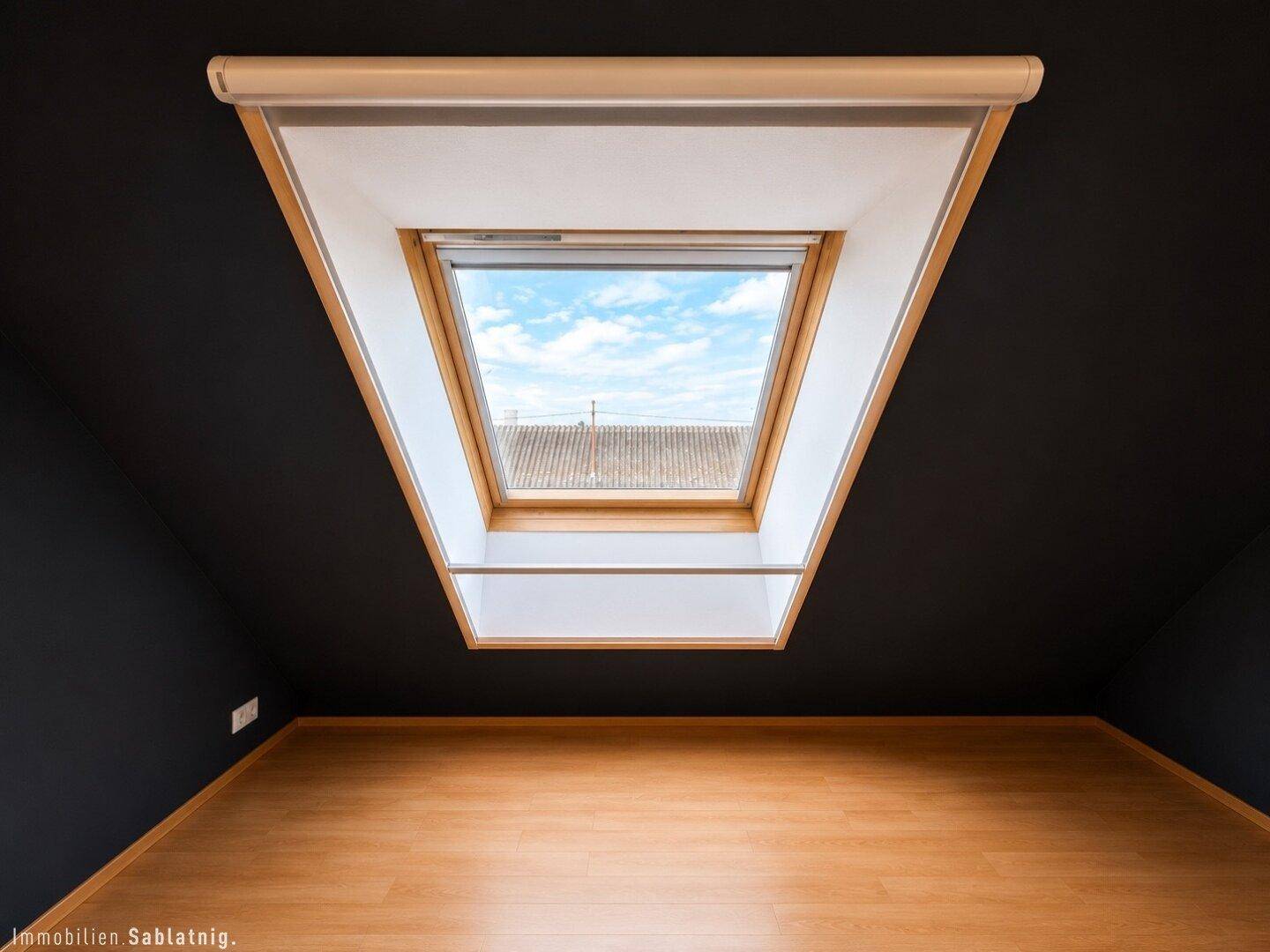 Dachfenster in einem Raum mit dunkler Decke und Holzboden.