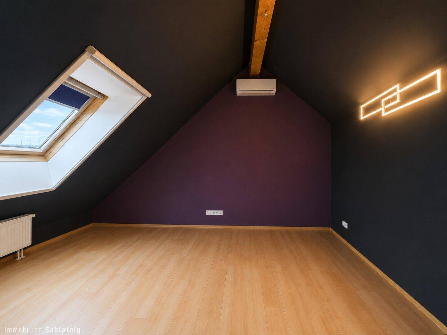 Schlafzimmer im Dachgeschoss mit dunklen Wänden, Holzboden und Dachfenster.