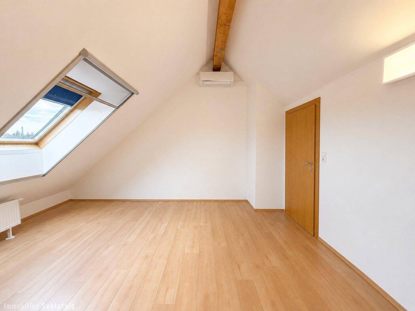 Helles Schlafzimmer im Dachgeschoss mit Holzboden, Dachfenster und Klimaanlage.