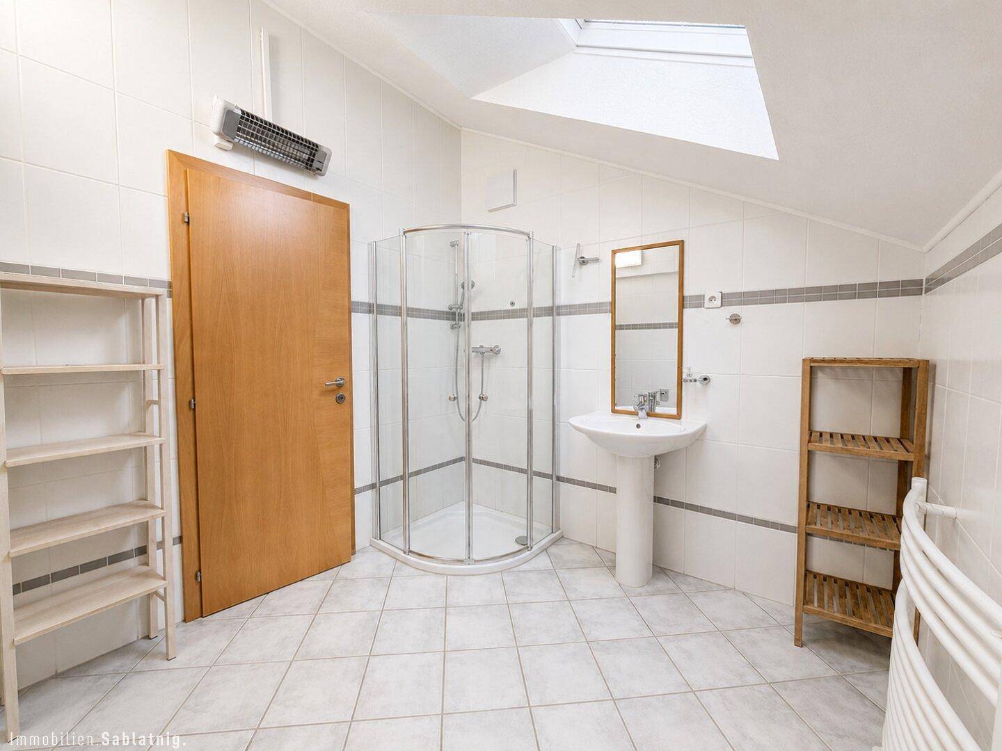 Helles Badezimmer mit Dusche, Waschbecken und Dachfenster.