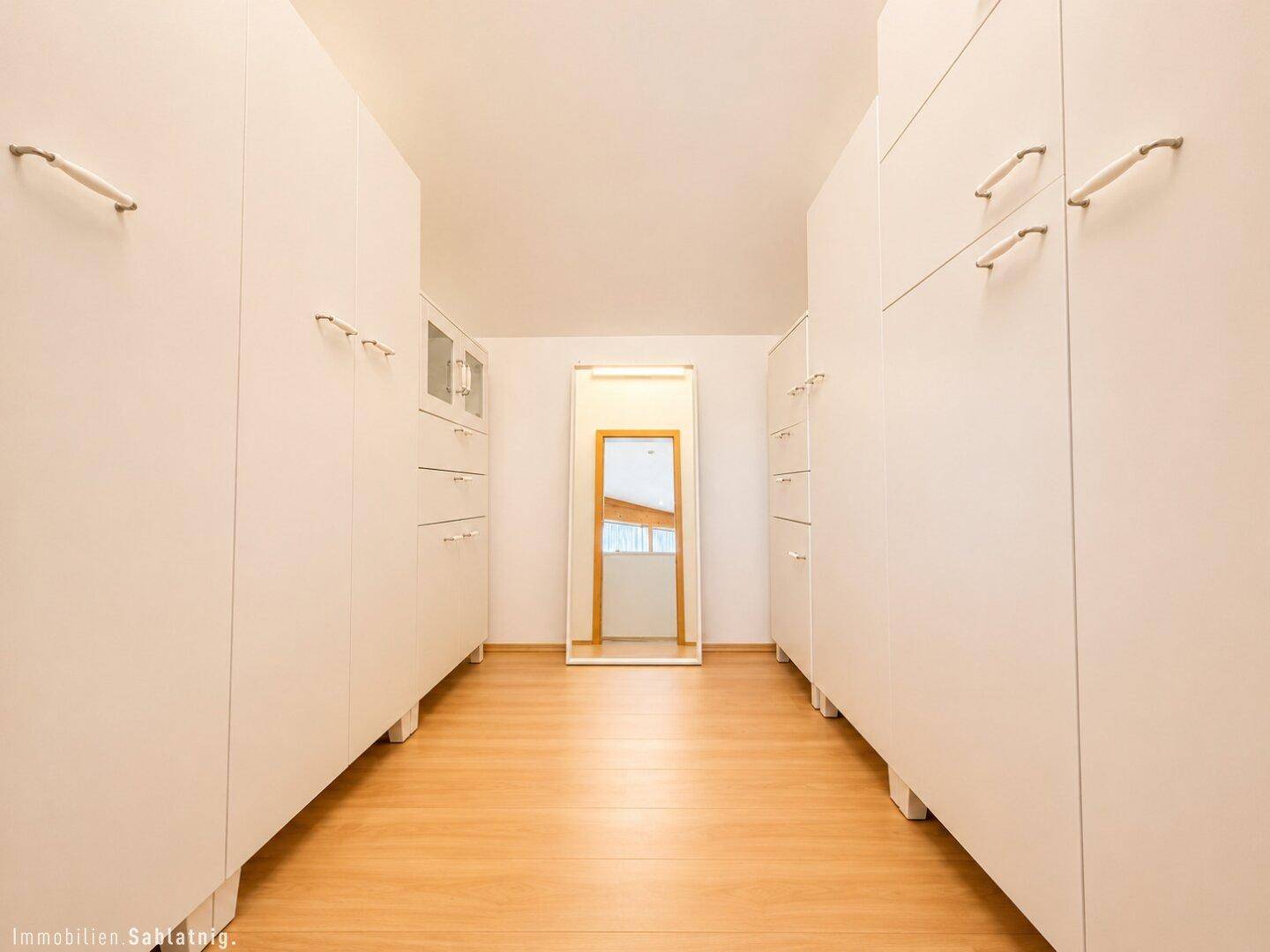 Geräumiger begehbarer Kleiderschrank mit vielen weißen Schränken und Spiegel.