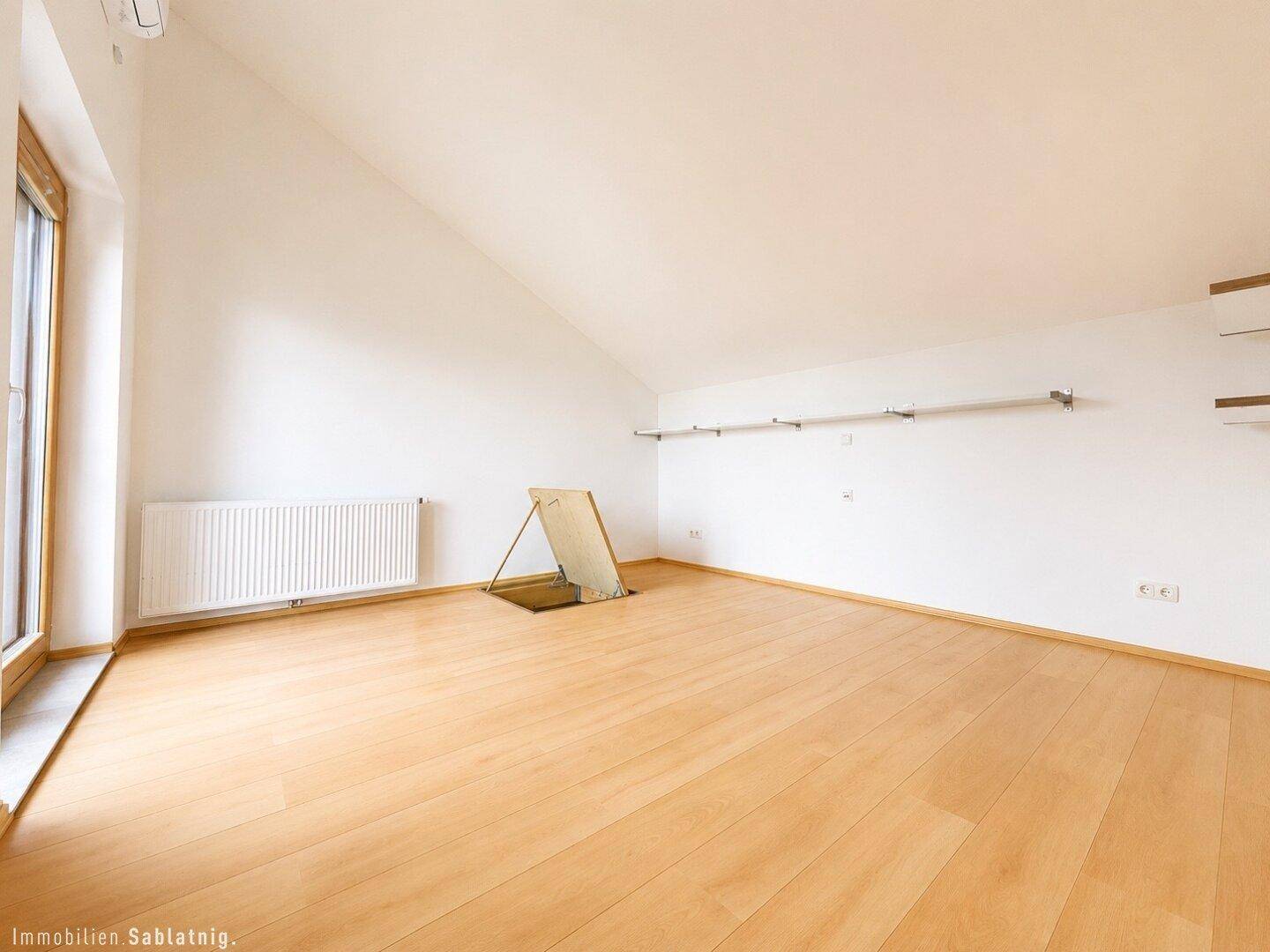 Geräumiger Dachboden mit Holzboden, schrägen Wänden und Heizkörper.