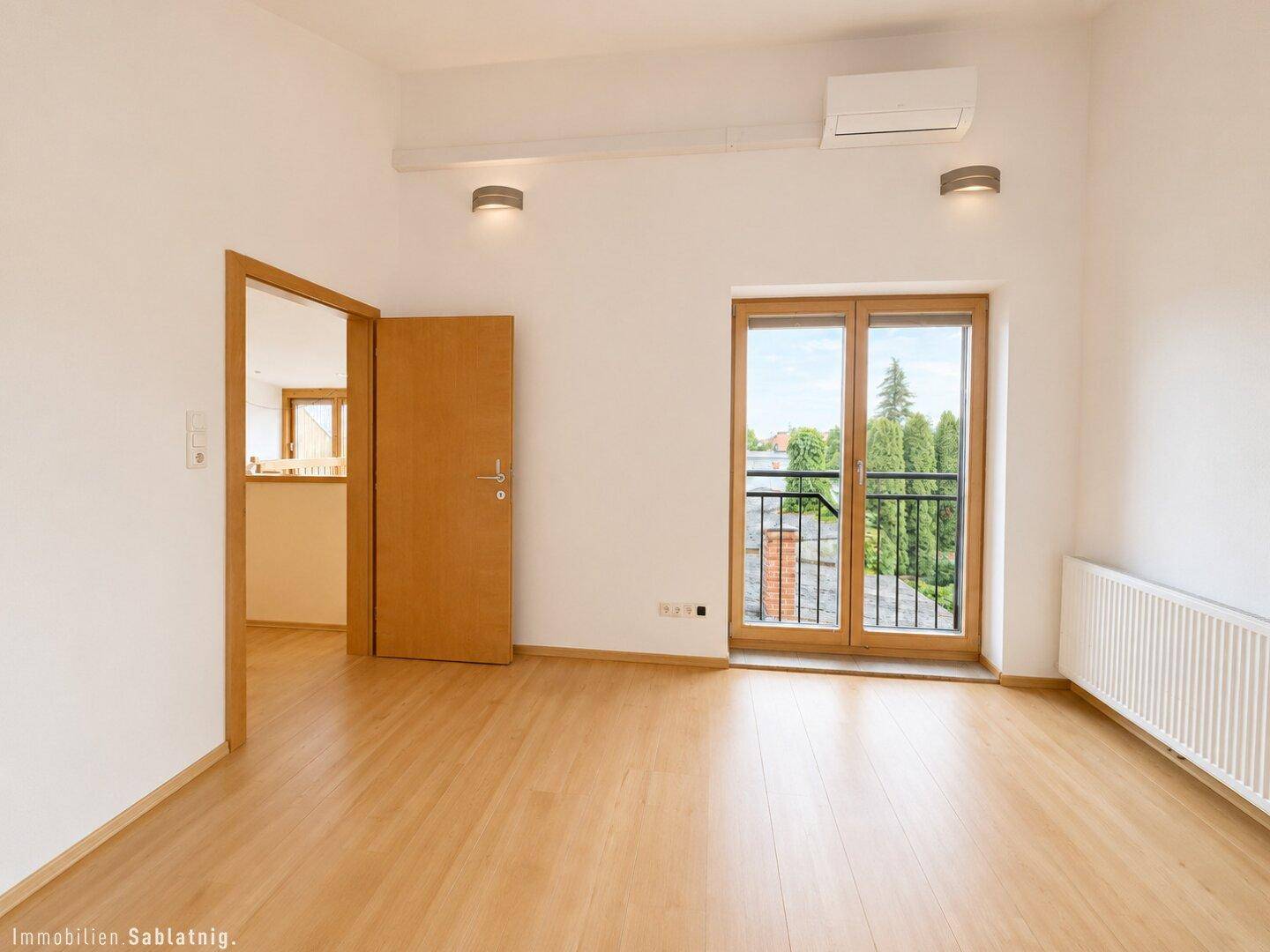 Helles Schlafzimmer mit Holzboden, Klimaanlage und französischem Balkon.