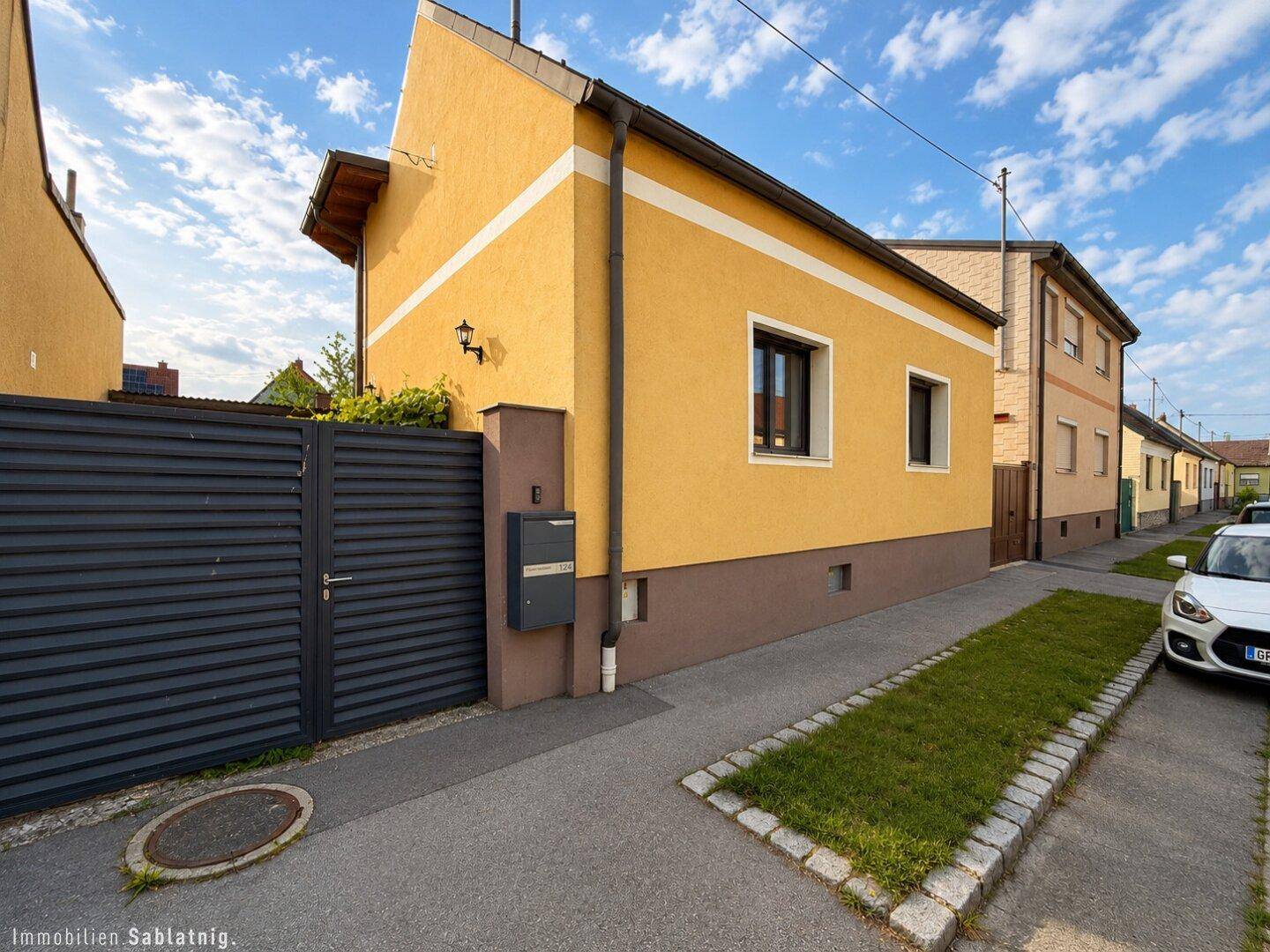 Straßenansicht des Hauses mit gelber Fassade, dunklem Tor und gepflegtem Vorgartenbereich.