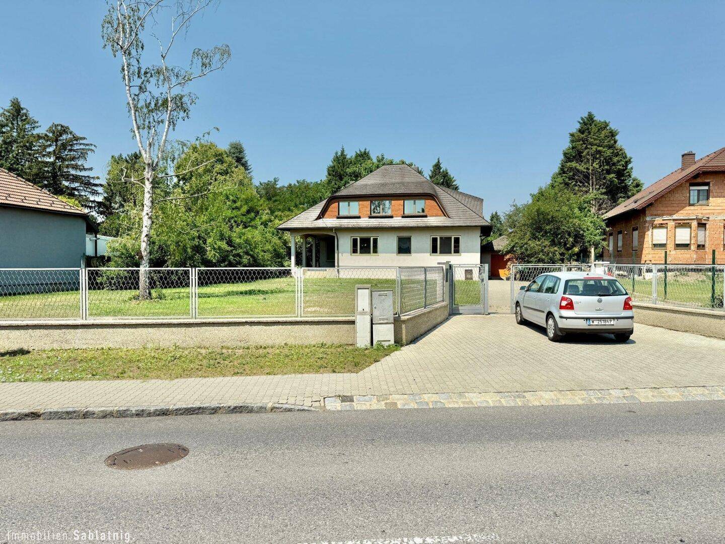 Straßenansicht des Hauses mit Vorgarten, Zaun, gepflasterter Einfahrt und parkendem Auto.