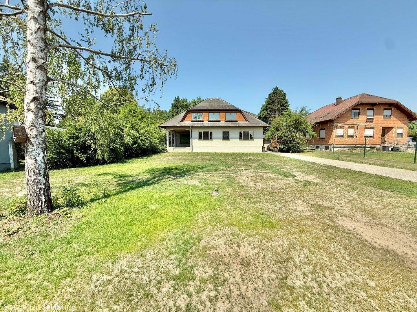 Vorderansicht des Hauses von der Rasenfläche aus, mit Zufahrt und Nachbarhäusern.
