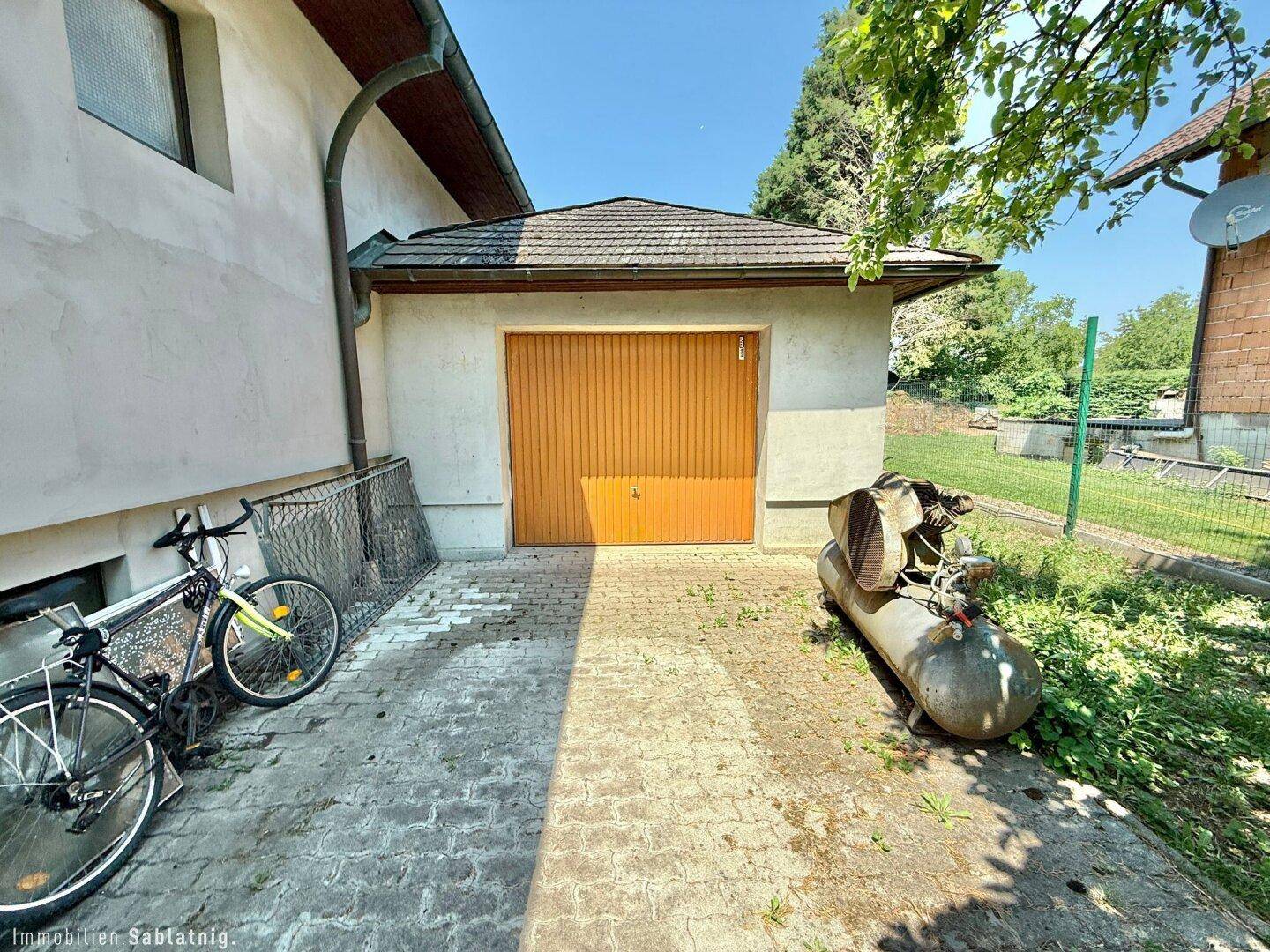 Freistehende Garage mit Holztor und gepflastertem Vorplatz, umgeben von Grün.
