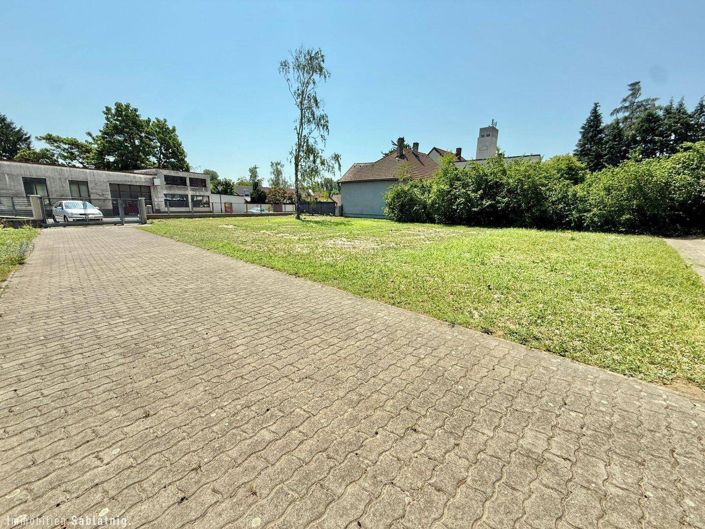 Große gepflasterte Fläche neben einer Rasenfläche mit einem Gebäude im Hintergrund.