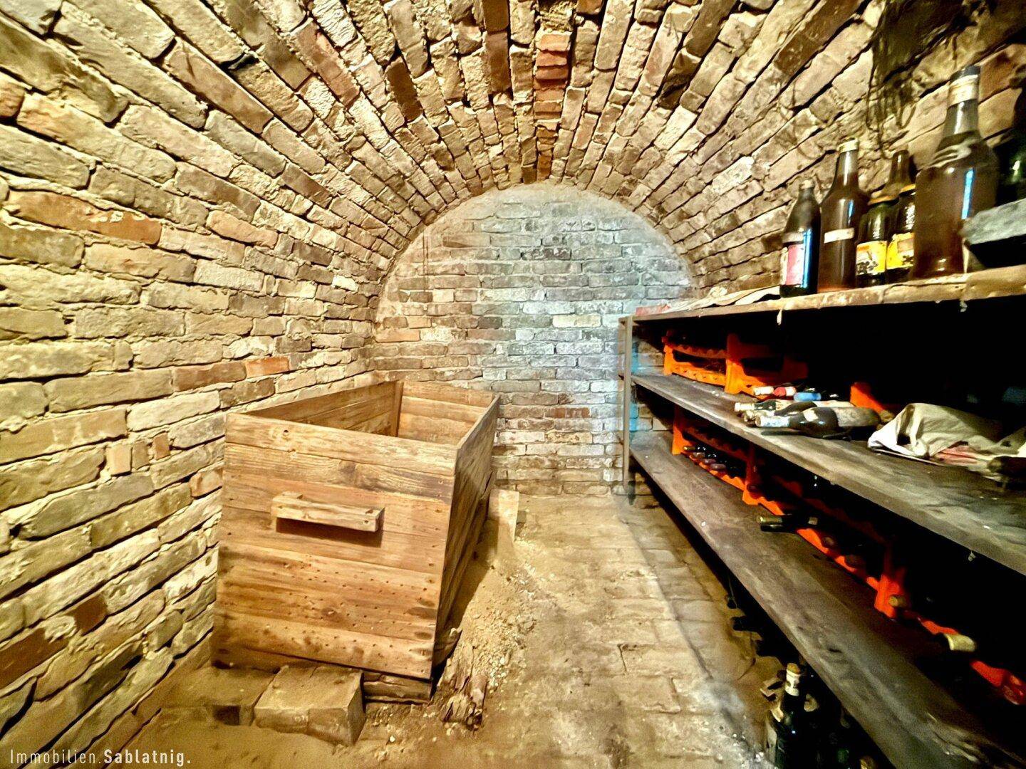 Historischer Weinkeller mit Ziegelwänden, Gewölbedecke und Holzregalen voller Flaschen.