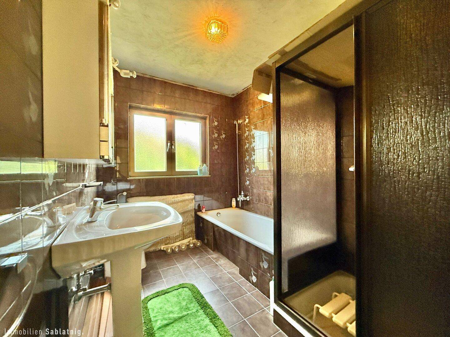 Badezimmer mit braunen Fliesen, Badewanne, Dusche und Fenster.