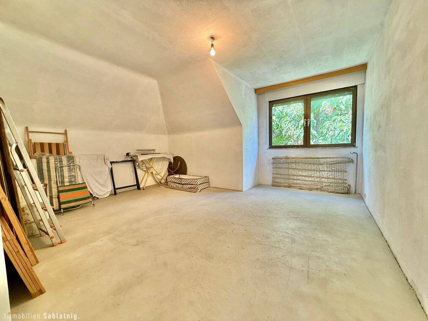 Helles Schlafzimmer im Dachgeschoss mit schrägen Wänden und Blick ins Grüne.