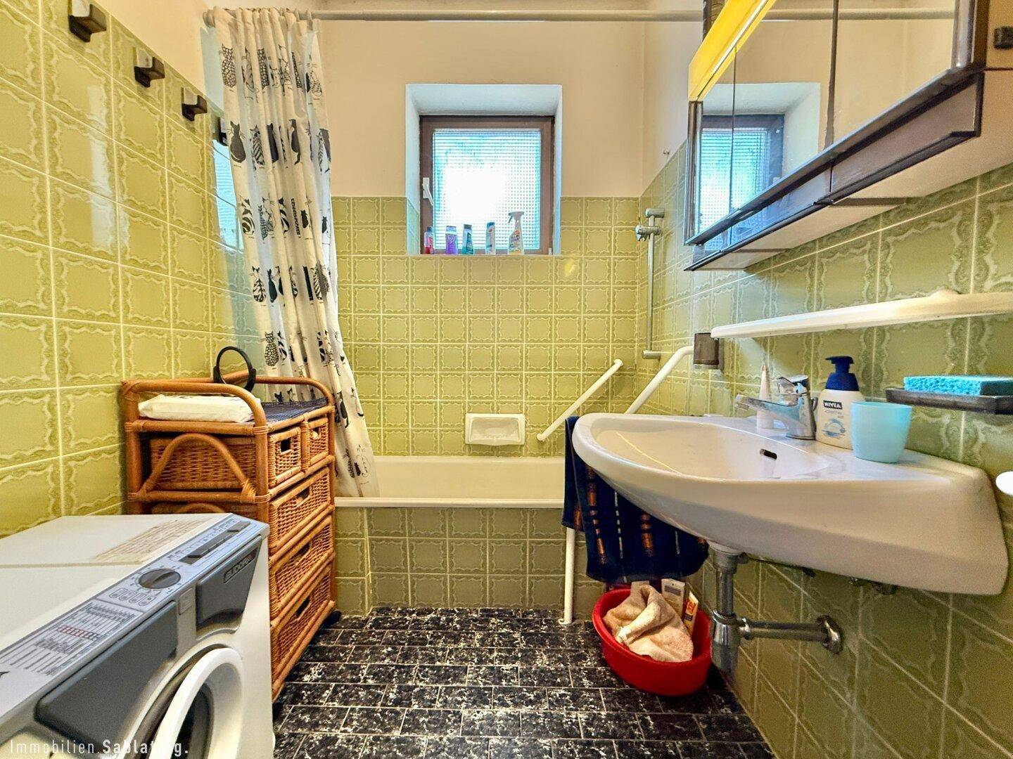 Badezimmer im 80er-Jahre-Stil mit grünen Fliesen, Badewanne und Waschmaschine.