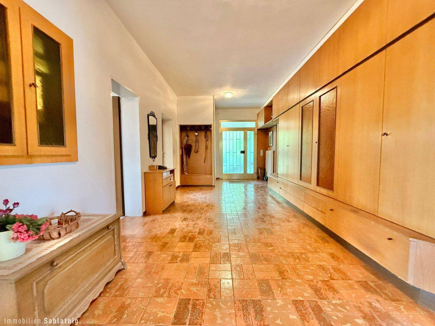 Breiter Eingangsbereich mit Holzschränken, Fliesenboden und Garderobe.