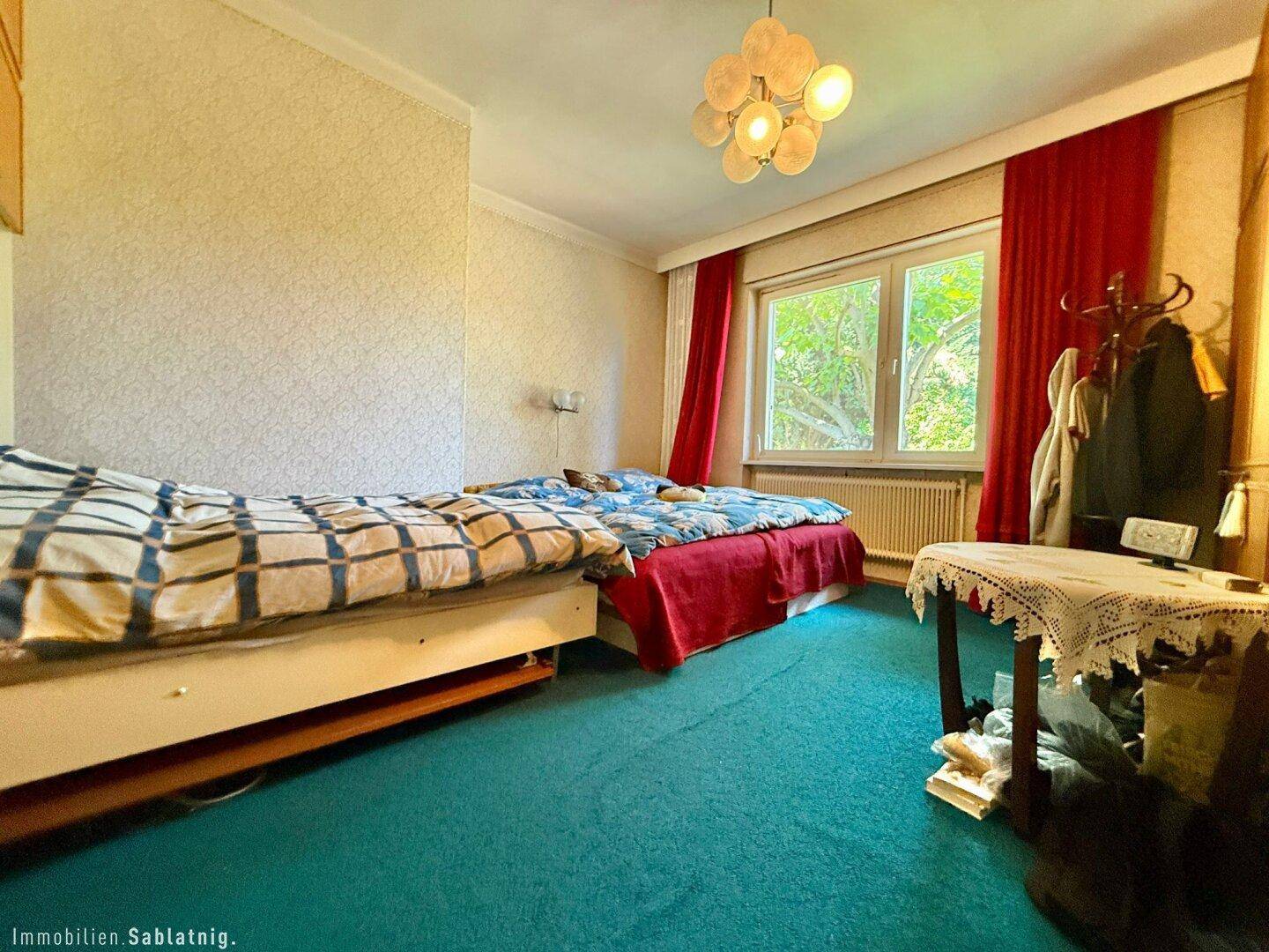Schlafzimmer mit zwei Betten, Teppichboden und roten Vorhängen.