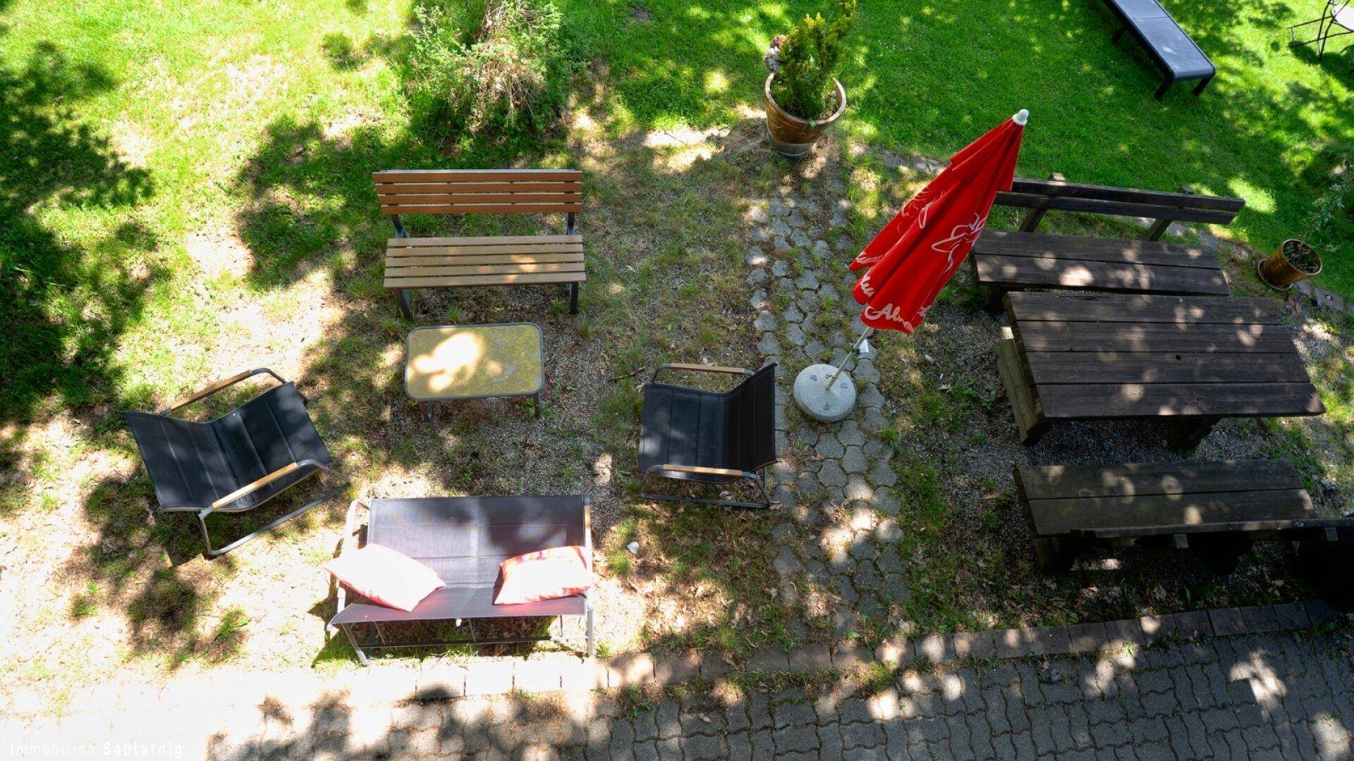 Vogelperspektive auf einen rustikalen Außenbereich mit Holzbänken, Tischen und einem Sonnenschirm.