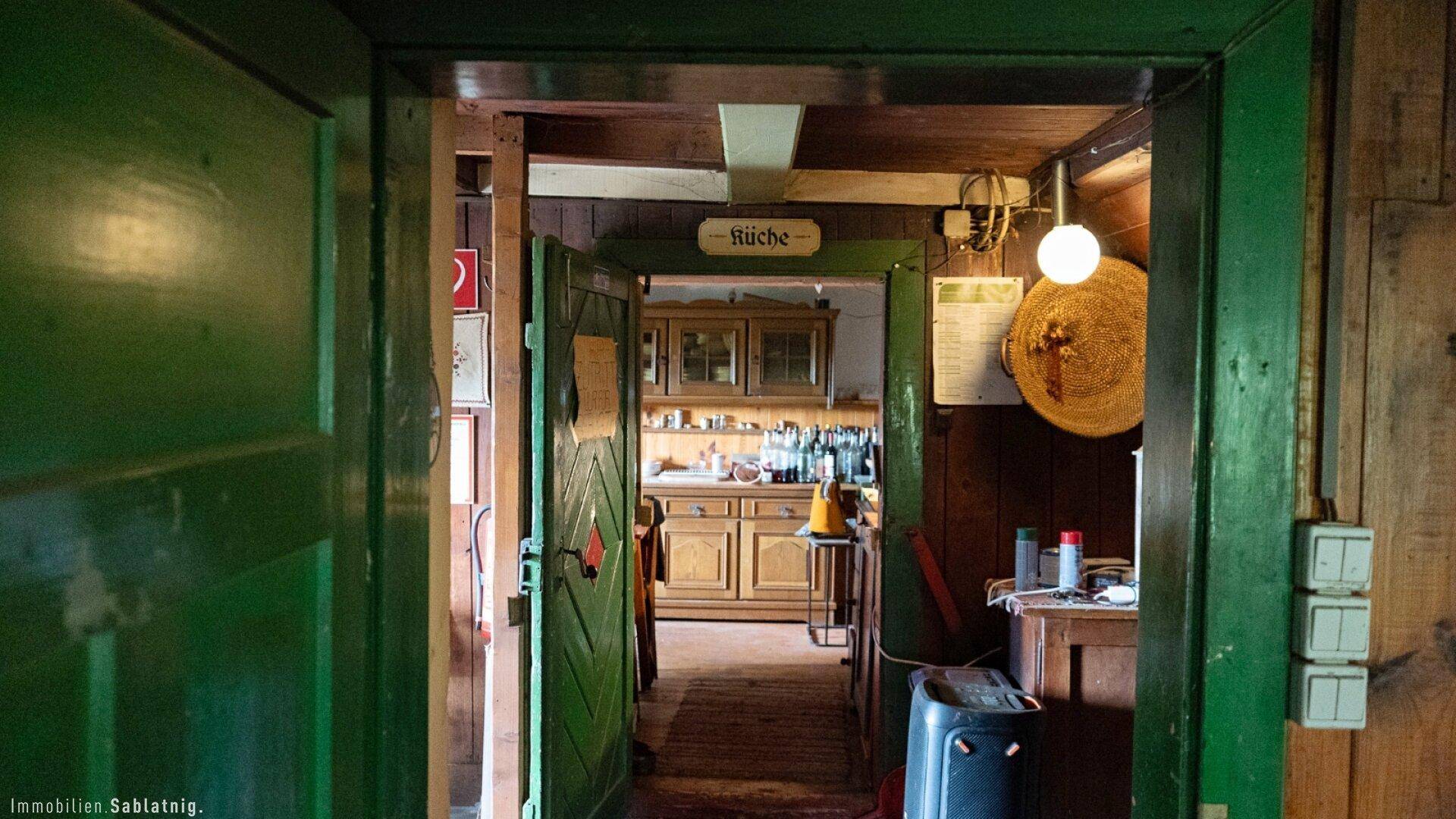 Blick durch eine offene Tür in eine rustikale Küche mit Holzschränken und traditioneller Einrichtung.