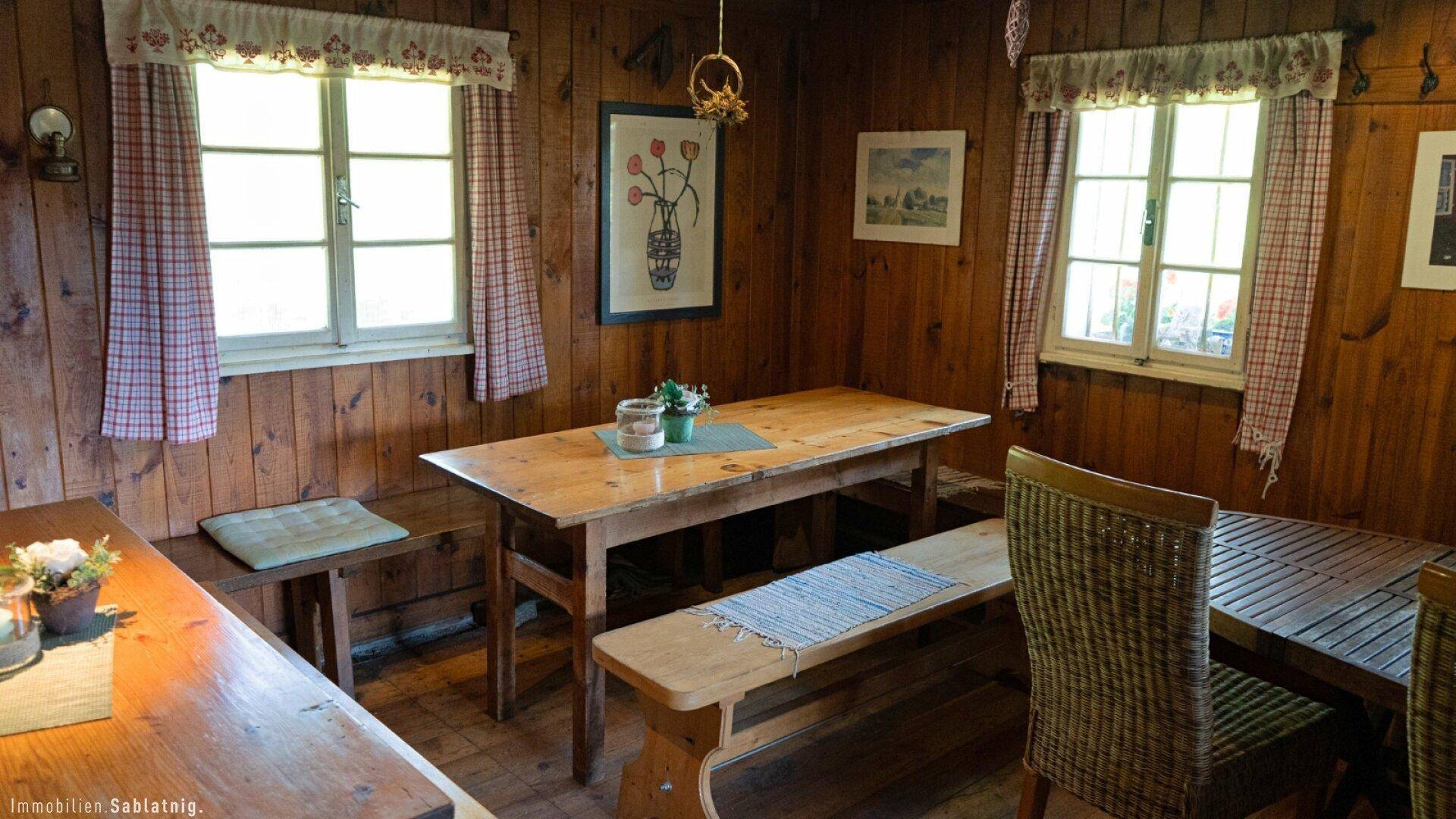 Detailansicht eines rustikalen Esstisches mit Holzbänken und karierten Vorhängen.