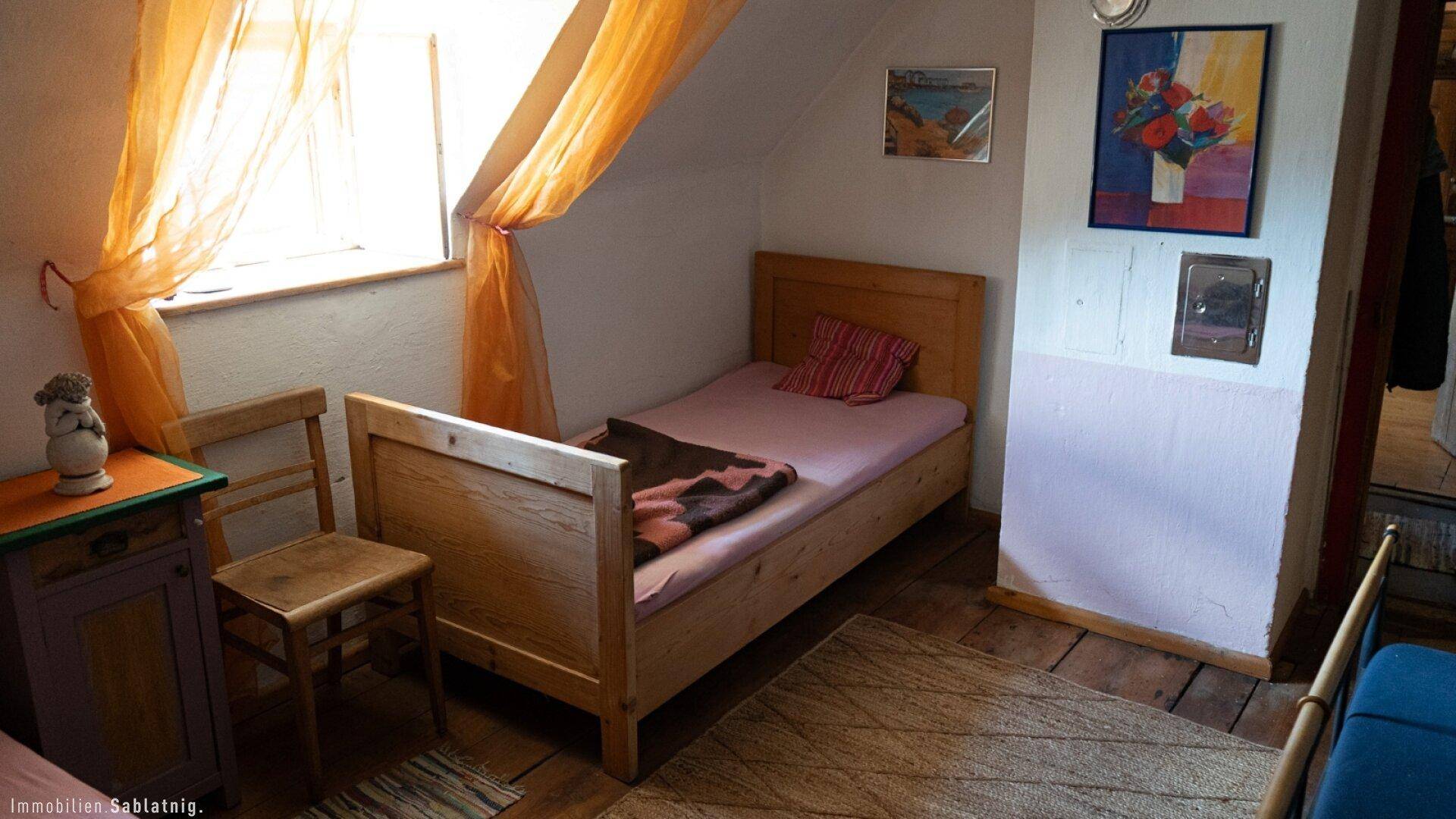 Helles Schlafzimmer im Dachgeschoss mit Einzelbett, Holzboden und schrägen Wänden.