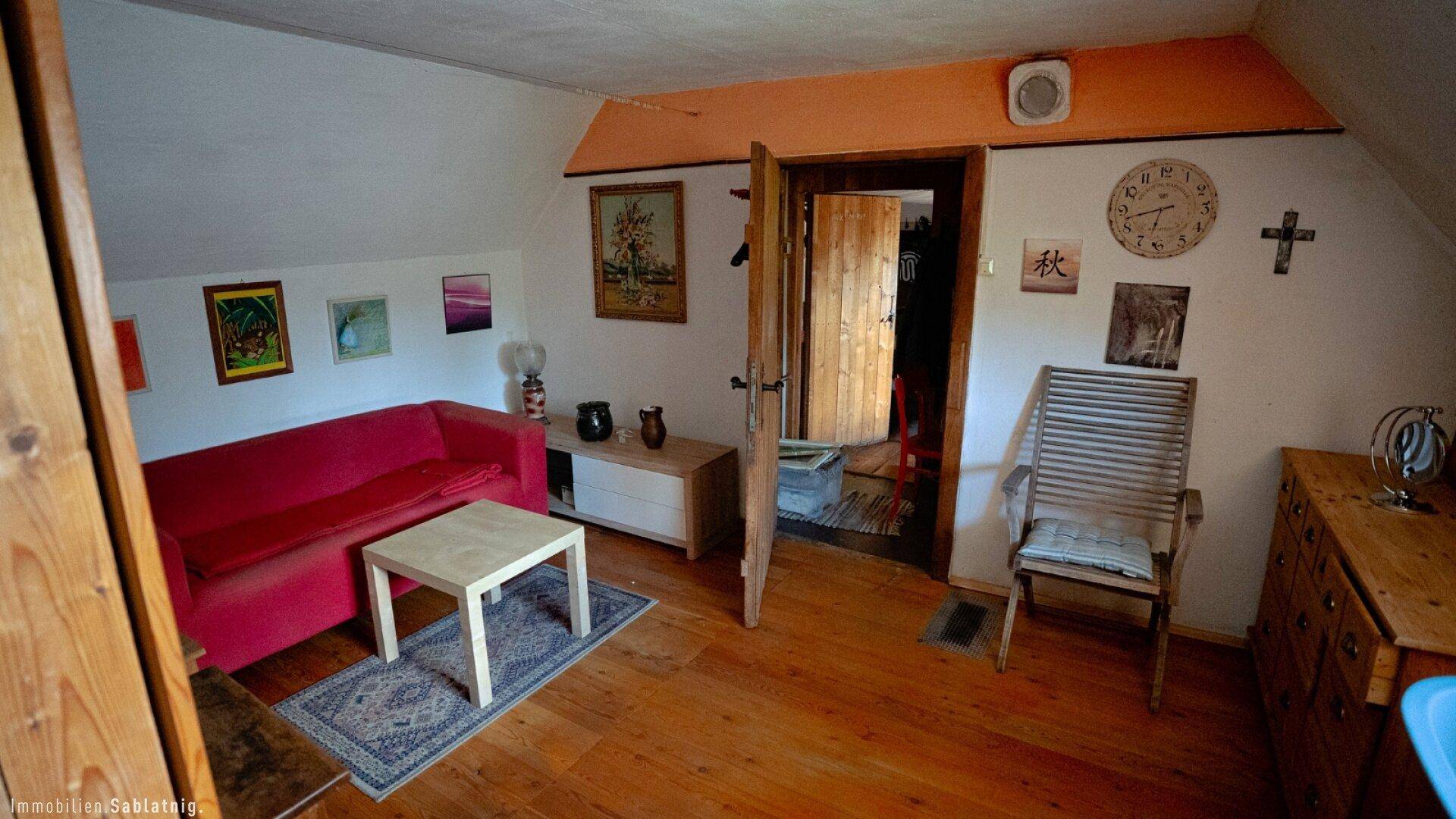 Gemütlicher Wohnbereich im Dachgeschoss mit rotem Sofa, Holzboden und rustikaler Dekoration.