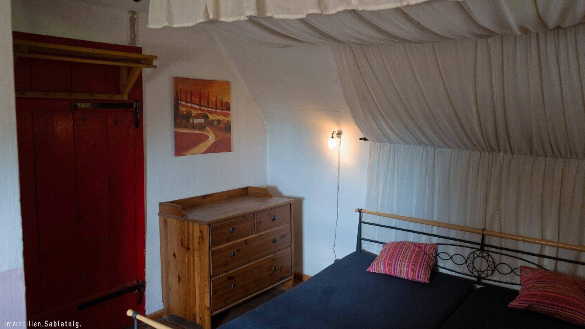Schlafzimmer mit Holzboden, Kommode und einem Bett mit schlichtem Metallrahmen.