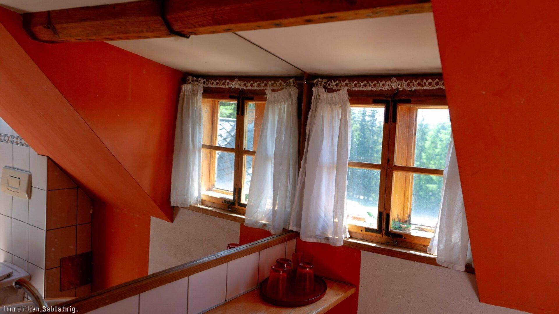 Kleiner Raum mit orangefarbenen Wänden, Holzfenstern und einem Waschbeckenbereich.